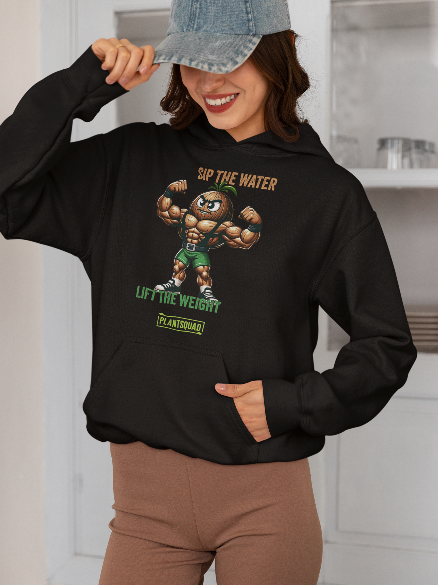 A Plantsquad Coconut "Sip The Water Lift The Weight" - Unisex Hoodie featuring a muscular cartoon nut flexing its biceps. Above the character, the text reads "SIP THE WATER." Below, it says "LIFT THE WEIGHT" with "PLANTSQUAD" at the bottom. Made from cozy fabric, it's perfect for anyone embracing a vegan lifestyle and passionate about weight lifting.