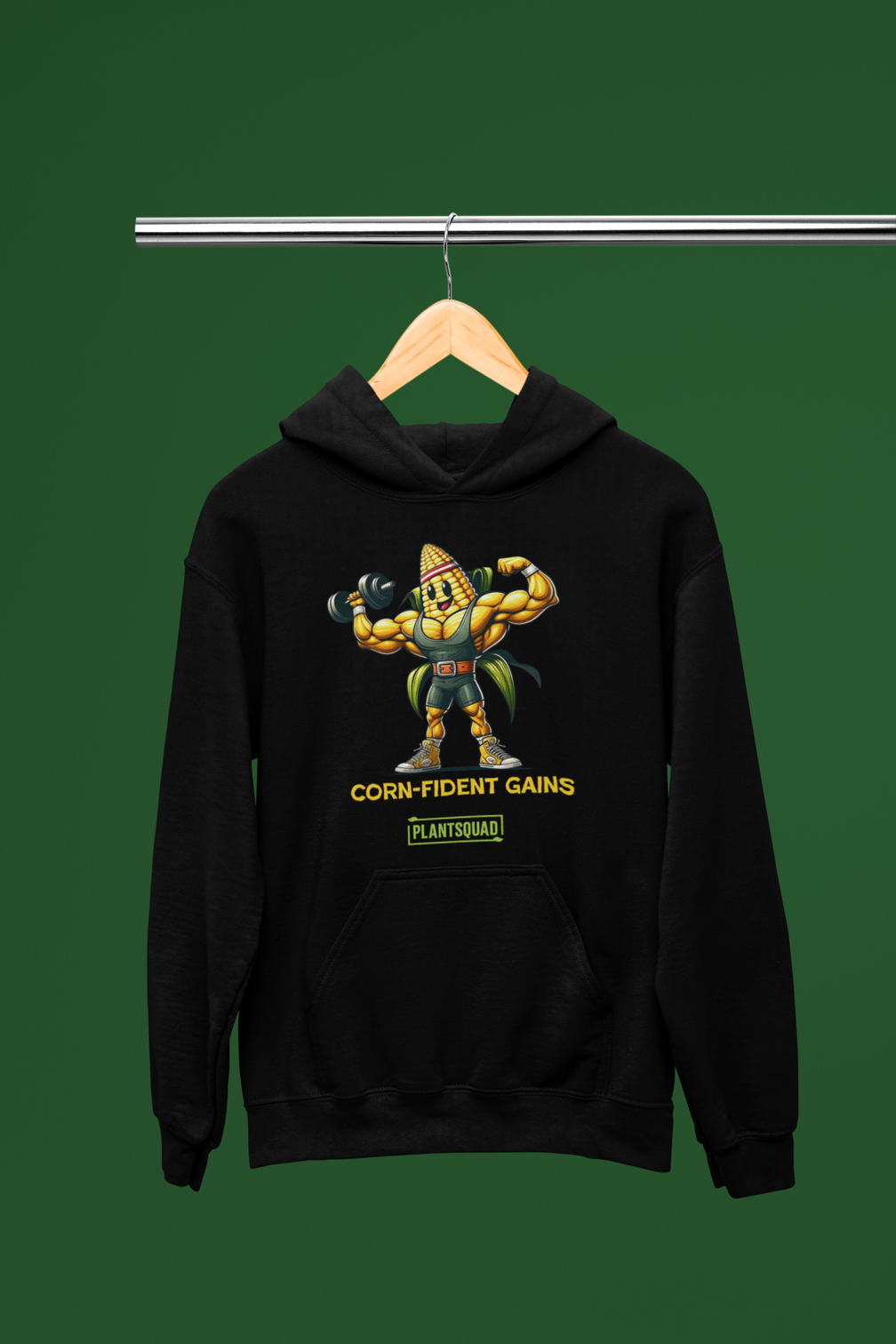 Black hoodie featuring a muscular anthropomorphic corn cob character flexing its biceps. The text beneath the character reads "CORN-fident Gains" with "PLANTSQUAD" in a green box below. Perfect for gym enthusiasts who embrace a plant-based lifestyle, this Plantsquad Corn "Corn-fident Gains" - Unisex Hoodie exudes confidence with every wear.