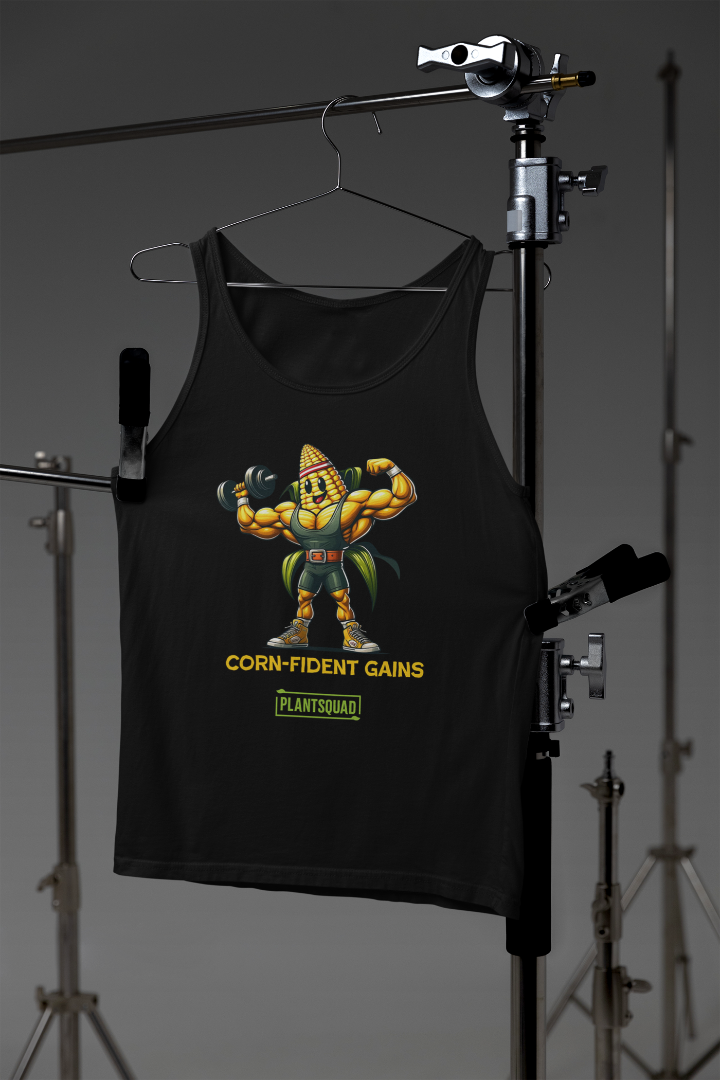 A black gym tank top featuring a muscular cartoon corn on the cob lifting a dumbbell. The corn character has sunglasses and a confident expression. The text below reads "CORN-FIDENT GAINS" and "PLANTSQUAD." Perfect for those seeking vegan workout clothes with style, this is the Plantsquad Corn "Corn-fident Gains" - Unisex Tank Top!