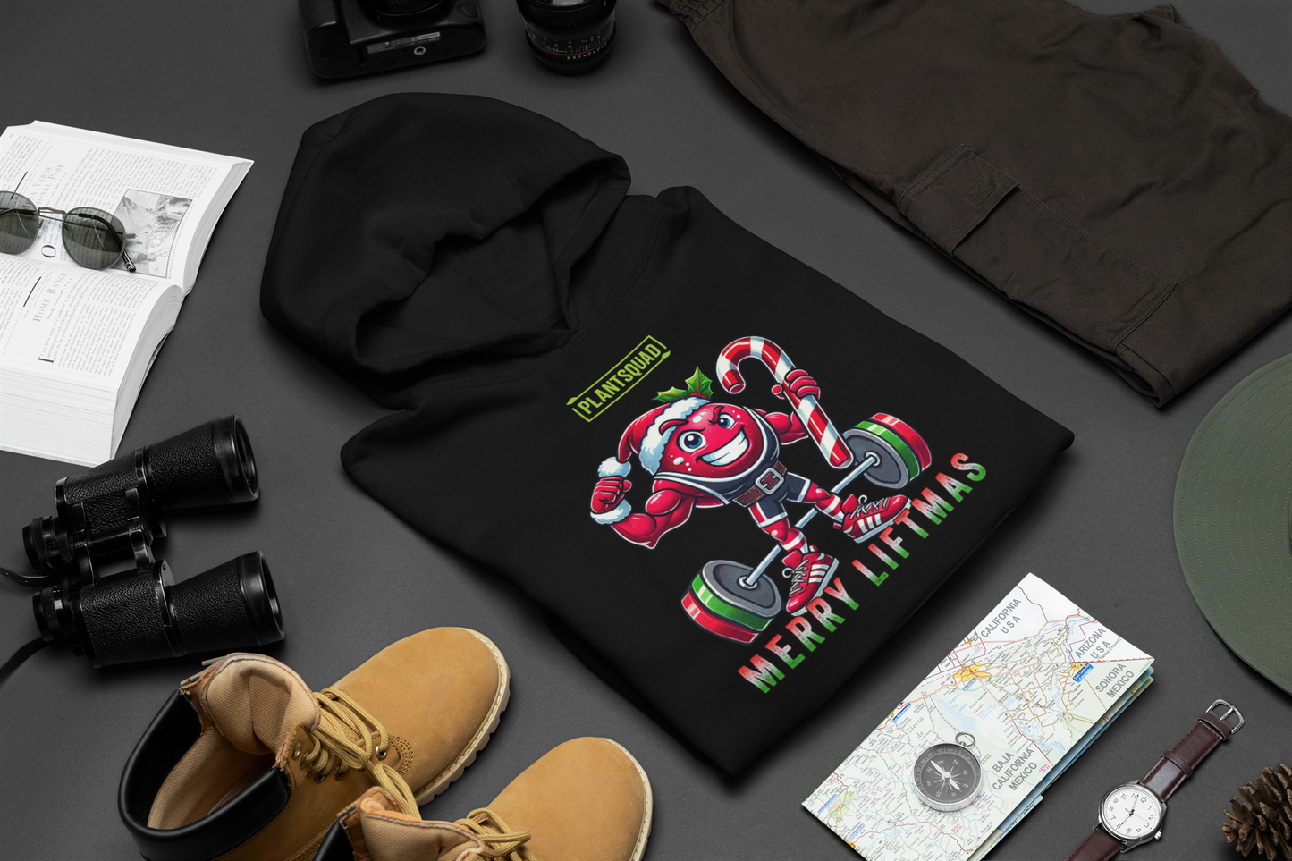 A folded t-shirt on a table with a muscled cranberry cartoon character flexing its arms holding a candy cane.  A small green logo "PLANTSQUAD" appears above the character, "MERRY LIFTMAS" below. Perfect for those embracing a plant-based or vegan lifestyle that are into fitness