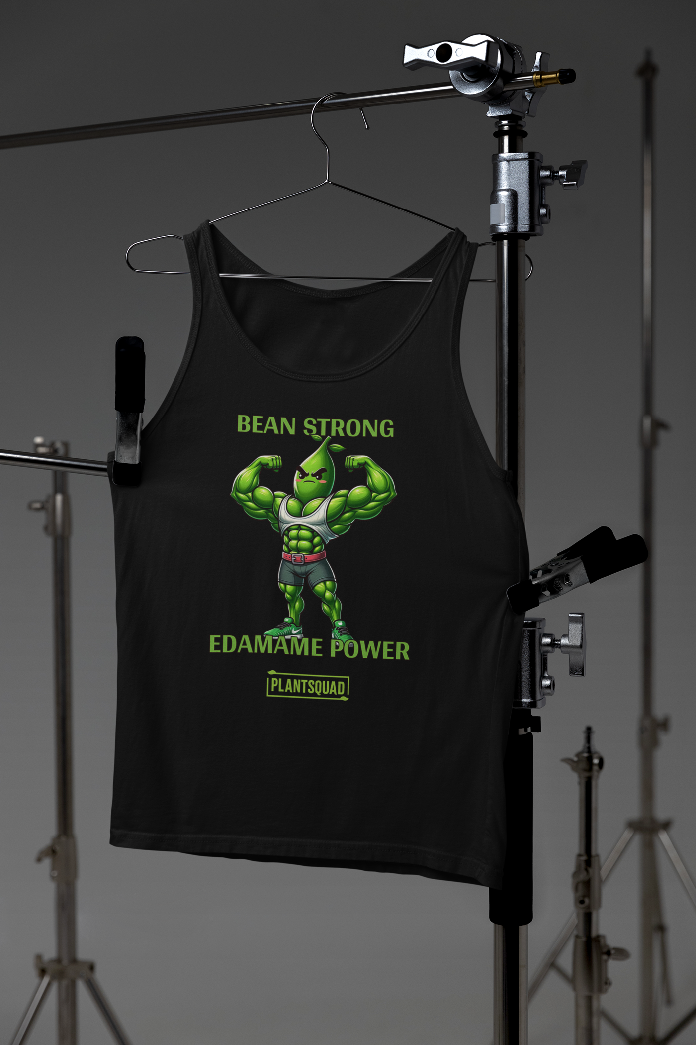 A black Plantsquad Edamame "Bean Strong Edamame Power" - Unisex Tank Top featuring an illustration of an anthropomorphic edamame bean flexing its arm muscles, perfect for gym enthusiasts. Above it in green text, it says "BEAN STRONG," and below it, "EDAMAME POWER." At the bottom, there is a green logo with the text "PLANTSQUAD." Embrace the vegan lifestyle!