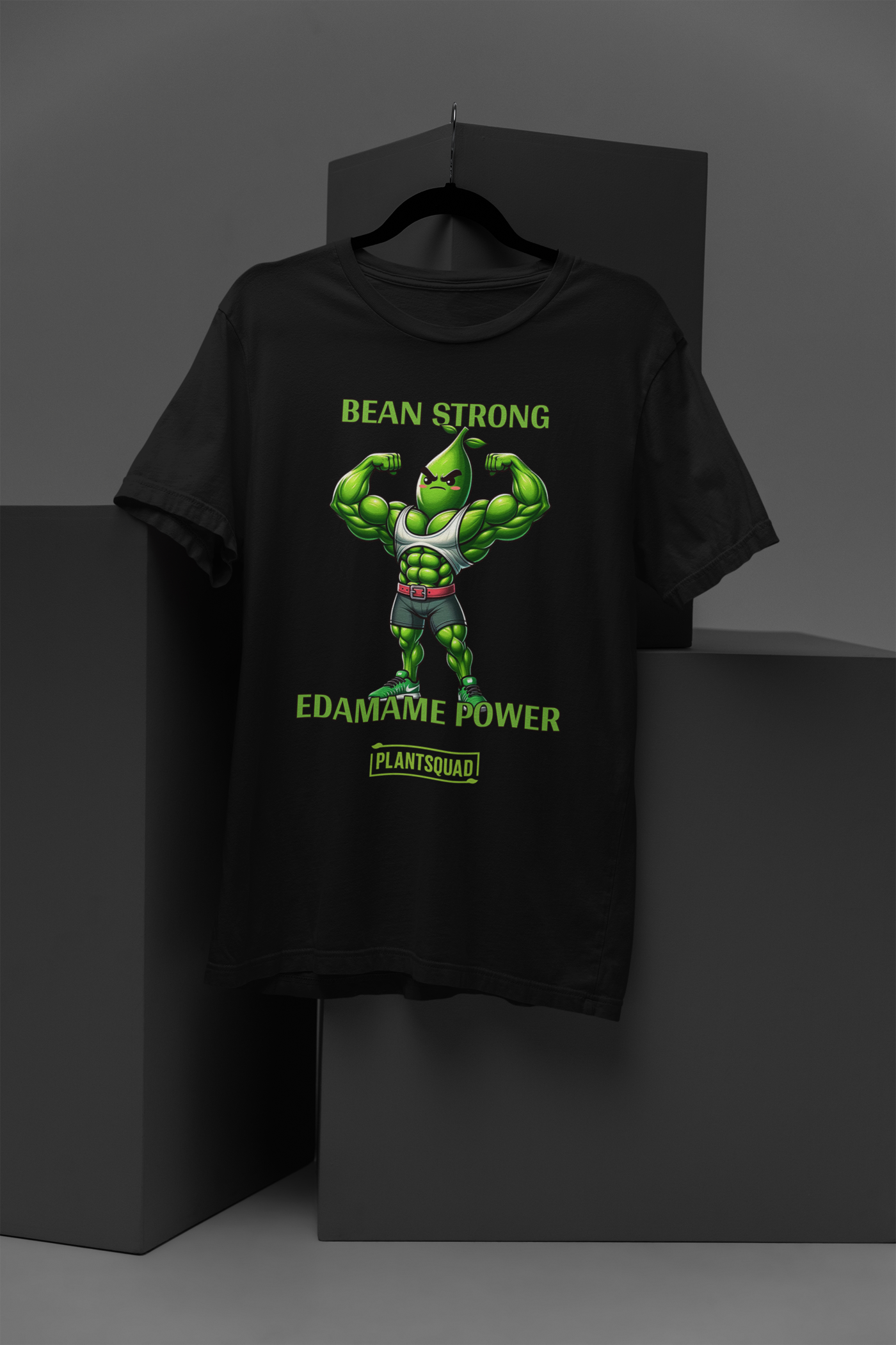 A Plantsquad Edamame "Bean Strong Edamame Power" - Unisex T-Shirt showcasing a cartoon edamame bean flexing its muscles. Above, the text reads "BEAN STRONG," with "EDAMAME POWER" below. At the bottom, "PLANTSQUAD" is featured within a green rectangular box, celebrating your love for plant-based strength.