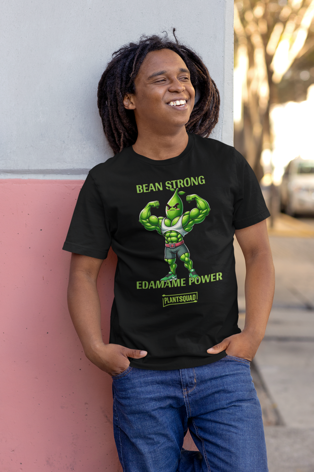 A Plantsquad Edamame "Bean Strong Edamame Power" - Unisex T-Shirt showcasing a cartoon edamame bean flexing its muscles. Above, the text reads "BEAN STRONG," with "EDAMAME POWER" below. At the bottom, "PLANTSQUAD" is featured within a green rectangular box, celebrating your love for plant-based strength.