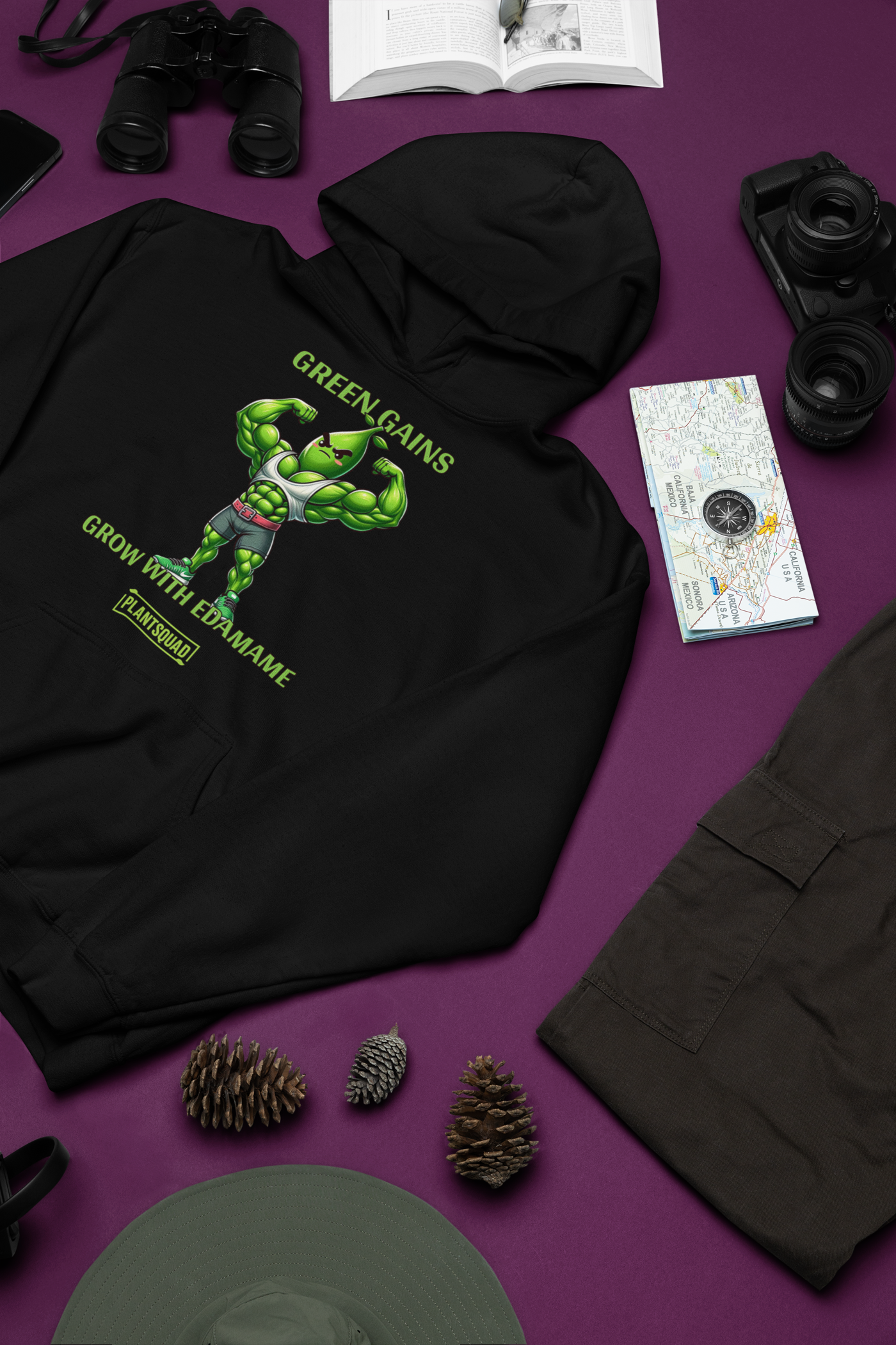 A Plantsquad Edamame "Green Gains Grow With Edamame" - Unisex Hoodie featuring a muscular, cartoon edamame bean character flexing its arms. The text above the character reads "GREEN GAINS," and below it reads "GROW WITH EDAMAME." Perfect for a Vegan lifestyle, the "PLANTSQUAD" logo is displayed at the bottom.