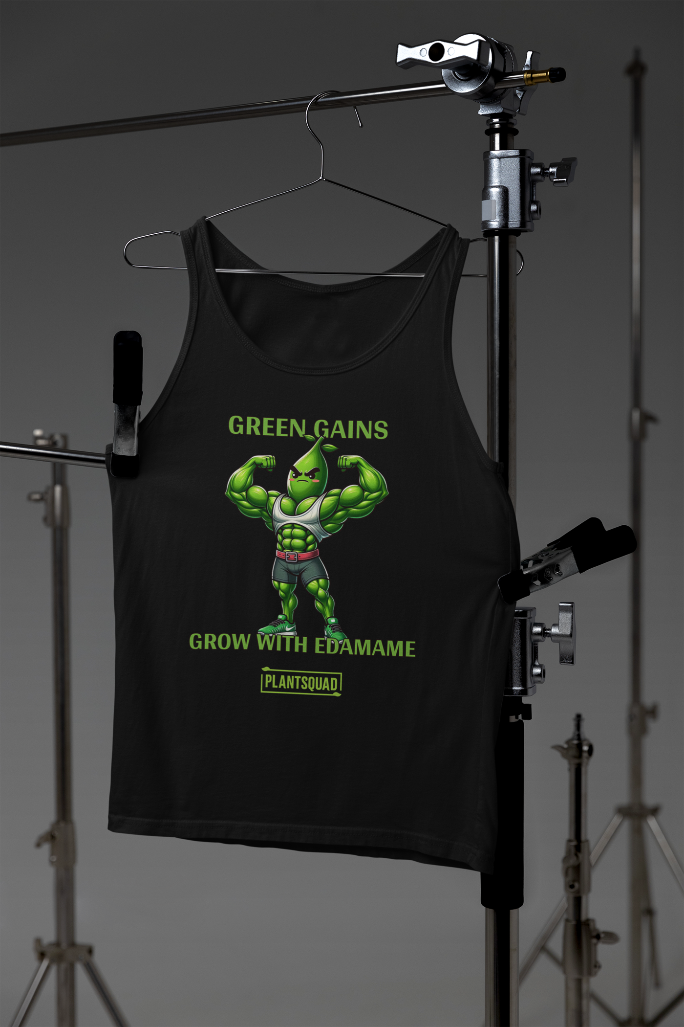 A black tank top showcases a muscly edamame bean character flexing, with the text "GREEN GAINS GROW WITH EDAMAME" above and below it, perfect for those embracing a plant-based lifestyle. Plantsquad Edamame "Green Gains Grow With Edamame" - Unisex Tank Top is marked at the bottom on a yellow tag.