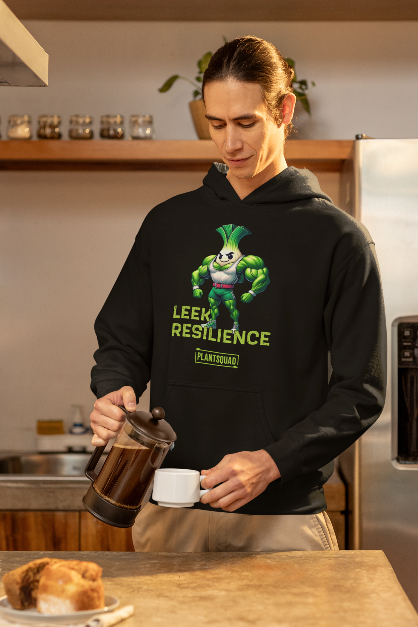 A black *Plantsquad Leek "Leek Resilience" - Unisex Hoodie* featuring an animated muscular leek character. The leek, with muscular arms and a confident pose, is accompanied by the text "Leek Resilience" above and "Plantsquad" below. Made from cozy fabric, this hoodie is perfect for those embracing a vegan lifestyle.