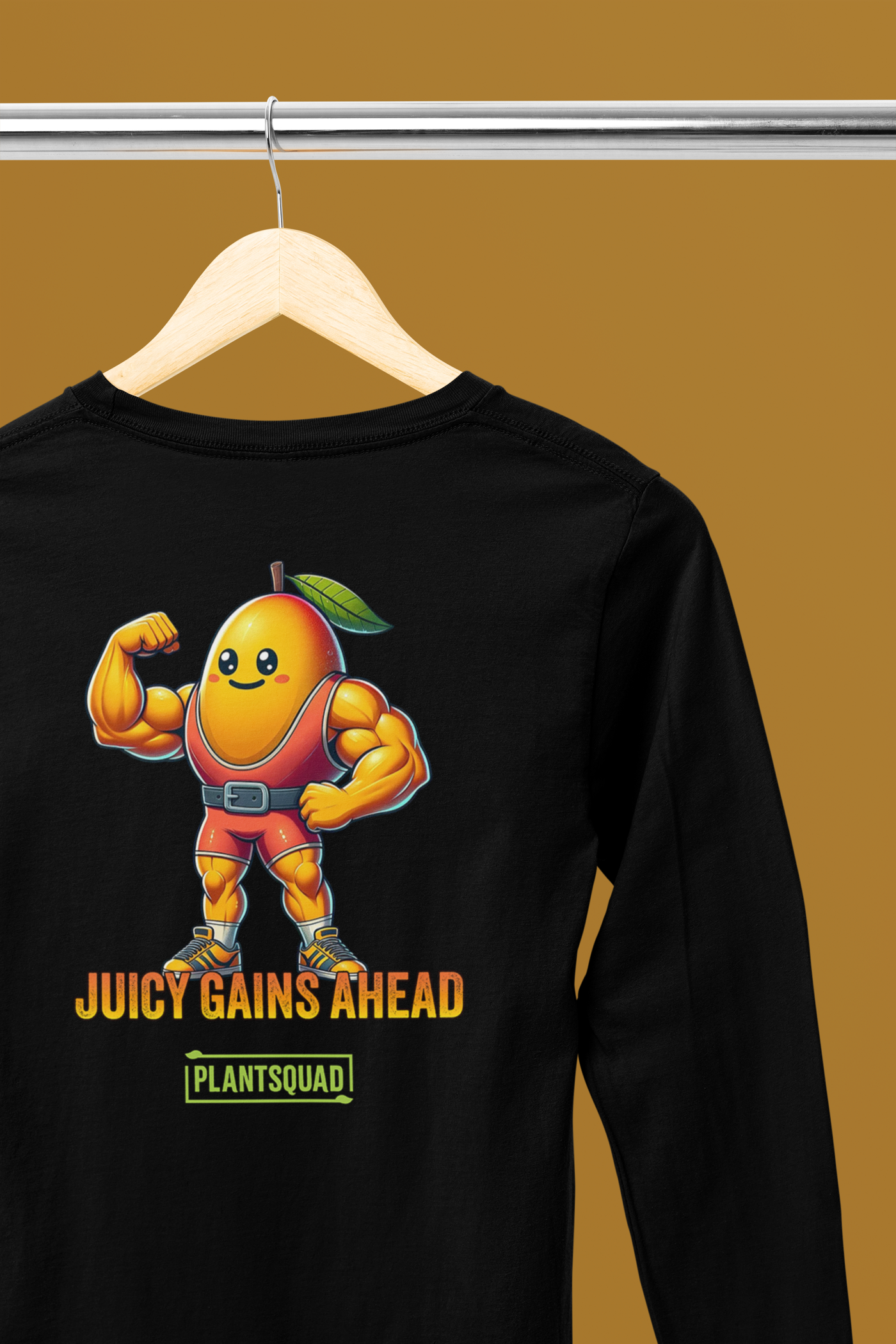 A black long-sleeve workout shirt featuring an illustration of a muscular anthropomorphic mango wearing a red leotard with green boots. Perfect for fitness enthusiasts, the text below reads "JUICY GAINS AHEAD" and "PLANTSQUAD," embracing the Vegan lifestyle. This is the Plantsquad Mango "Juicy Gains Ahead" - Unisex Long Sleeve T-Shirt.