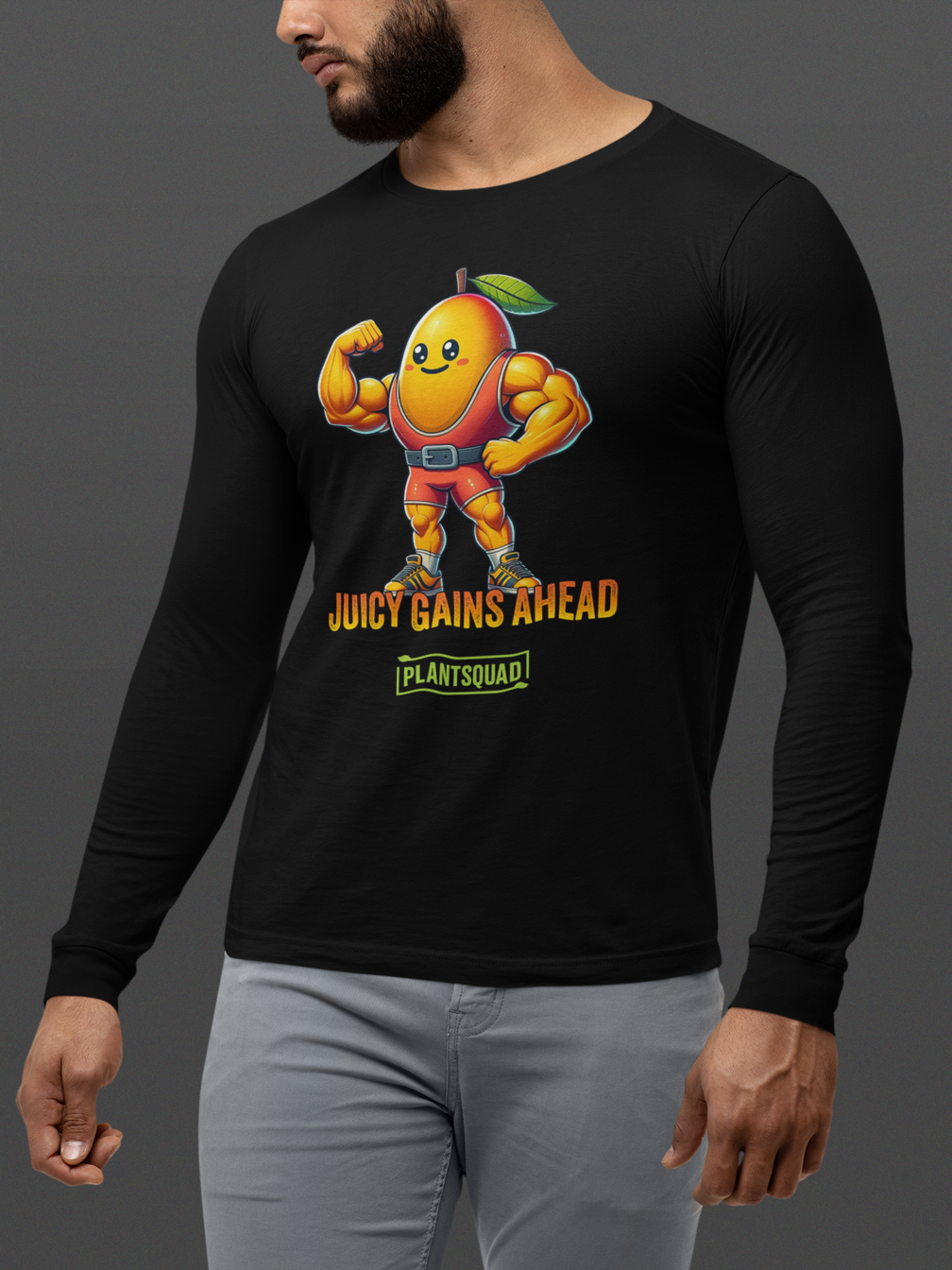 A black long-sleeve workout shirt featuring an illustration of a muscular anthropomorphic mango wearing a red leotard with green boots. Perfect for fitness enthusiasts, the text below reads "JUICY GAINS AHEAD" and "PLANTSQUAD," embracing the Vegan lifestyle. This is the Plantsquad Mango "Juicy Gains Ahead" - Unisex Long Sleeve T-Shirt.