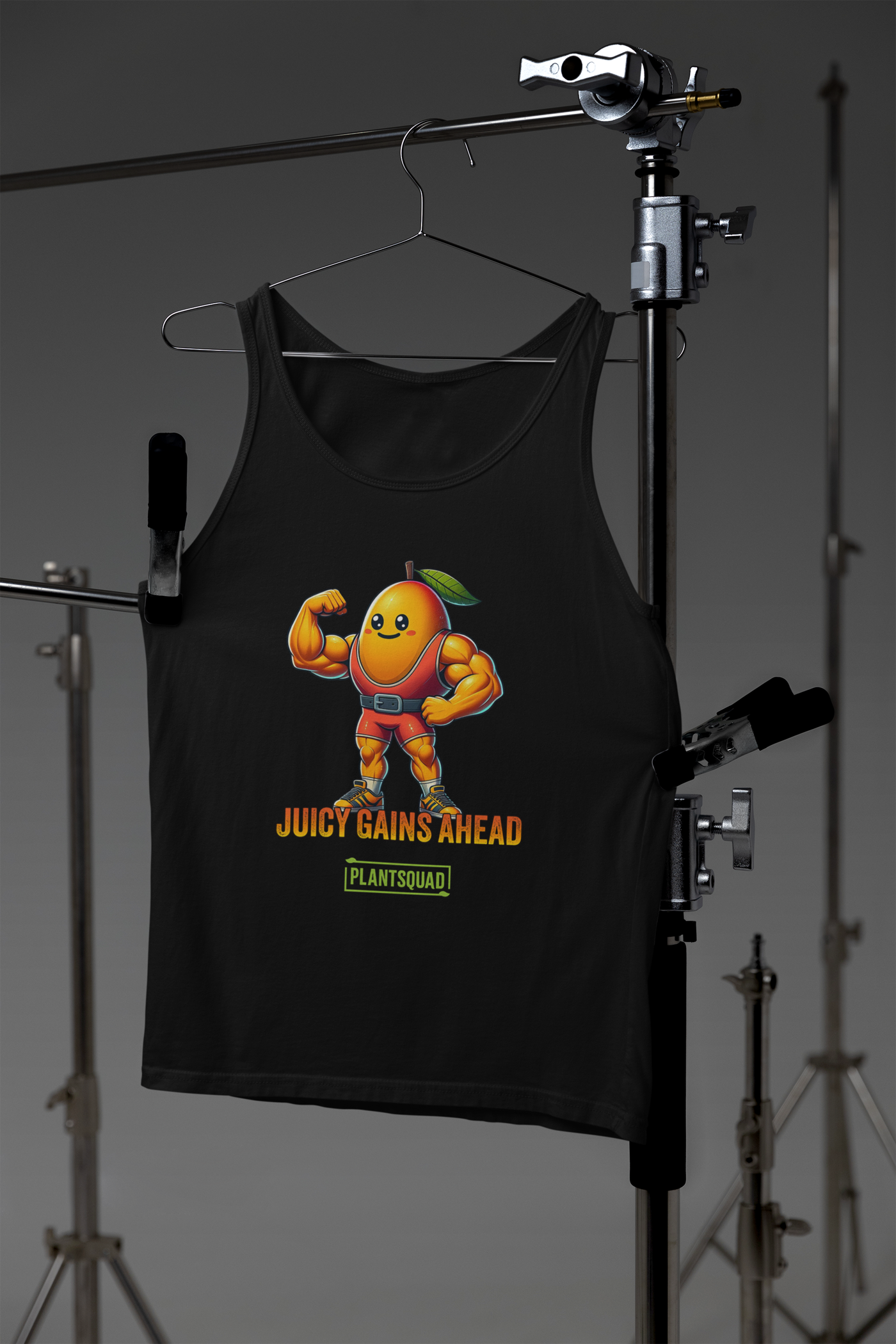 A black tank top crafted from breathable fabric, featuring a muscular, anthropomorphized mango with a leaf on its head, flexing its biceps. Below the mango, the text reads "JUICY GAINS AHEAD" in bold orange letters, with "PLANTSQUAD" written within a green box underneath—perfect for gym enthusiasts living a plant-based lifestyle. This is the Plantsquad Mango "Juicy Gains Ahead" - Unisex Tank Top.