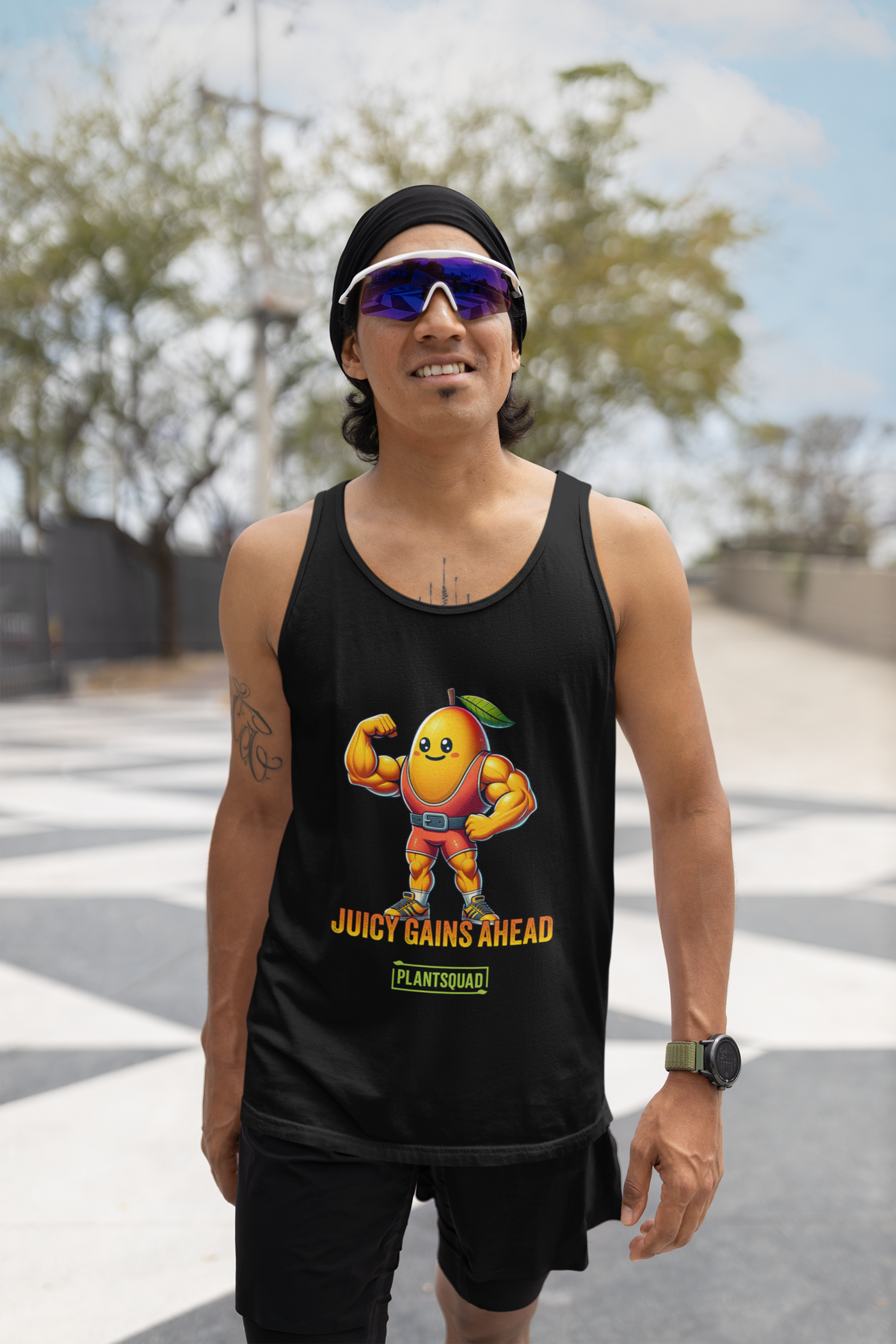 A black tank top crafted from breathable fabric, featuring a muscular, anthropomorphized mango with a leaf on its head, flexing its biceps. Below the mango, the text reads "JUICY GAINS AHEAD" in bold orange letters, with "PLANTSQUAD" written within a green box underneath—perfect for gym enthusiasts living a plant-based lifestyle. This is the Plantsquad Mango "Juicy Gains Ahead" - Unisex Tank Top.