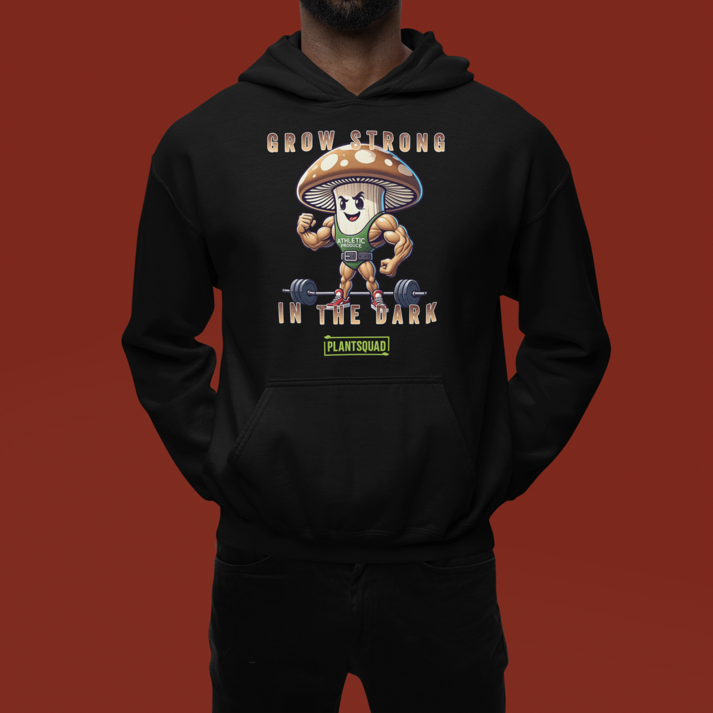 Plantsquad Mushroom "Grow Strong In The Dark" - Unisex Hoodie featuring an illustration of a muscular mushroom design wearing a tank top and lifting weights. Above the mushroom, text reads "GROW STRONG IN THE DARK," and below it, "PLANTSQUAD" is displayed on a green rectangular background. Perfect for those embracing a vegan lifestyle.