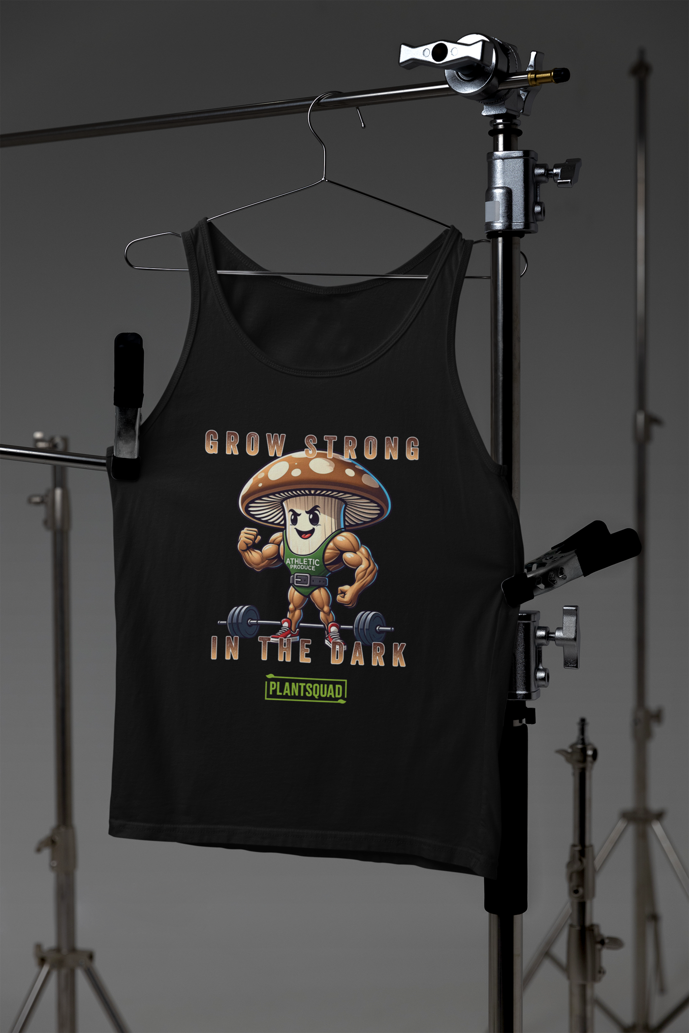 A black Plantsquad Mushroom "Grow Strong In The Dark" - Unisex Tank Top features a cartoon mushroom lifting weights with muscular arms. Text above and below the mushroom reads, "Grow Strong in the Dark - PlantSquad". Perfect for gym enthusiasts embracing a plant-based lifestyle, the mushroom sports a green athletic shirt with "ATHLETIC" on it.