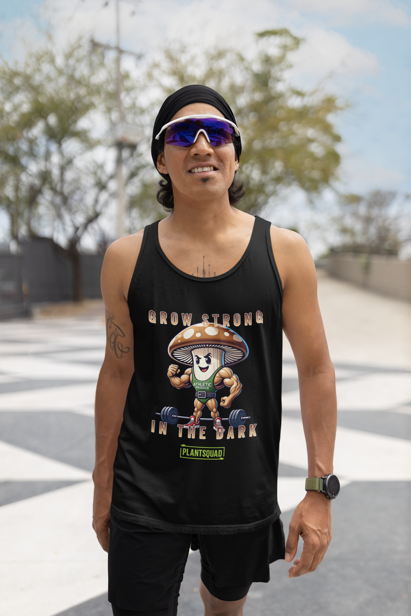 A black Plantsquad Mushroom "Grow Strong In The Dark" - Unisex Tank Top features a cartoon mushroom lifting weights with muscular arms. Text above and below the mushroom reads, "Grow Strong in the Dark - PlantSquad". Perfect for gym enthusiasts embracing a plant-based lifestyle, the mushroom sports a green athletic shirt with "ATHLETIC" on it.