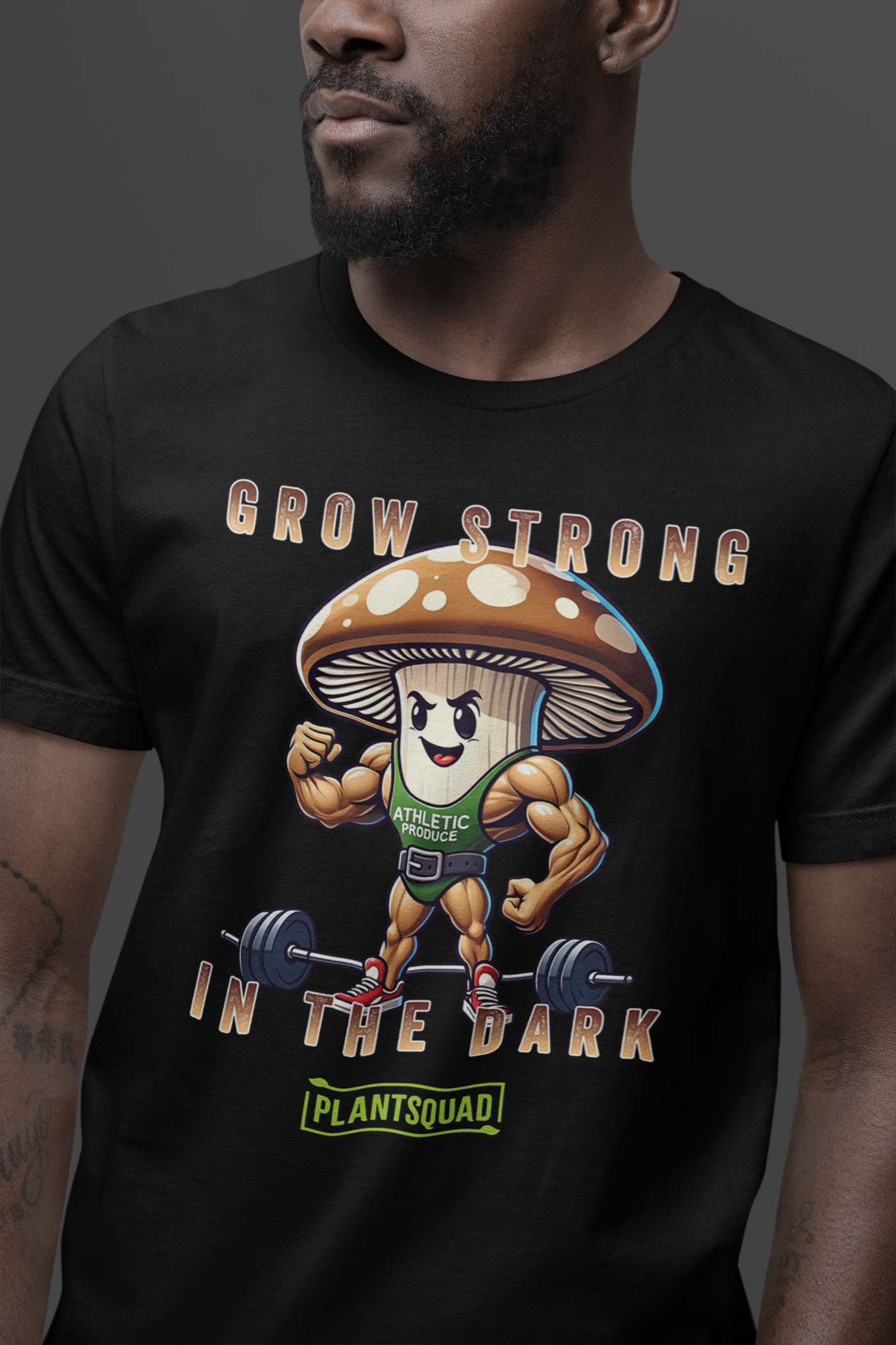 A Plantsquad Mushroom "Grow Strong In The Dark" - Unisex T-Shirt made of breathable fabric featuring a cartoon mushroom character with muscular arms and legs, flexing its biceps and standing in front of a barbell. The text above reads, "GROW STRONG IN THE DARK," and the text below reads, "PLANTSQUAD." Perfect for fitness enthusiasts.