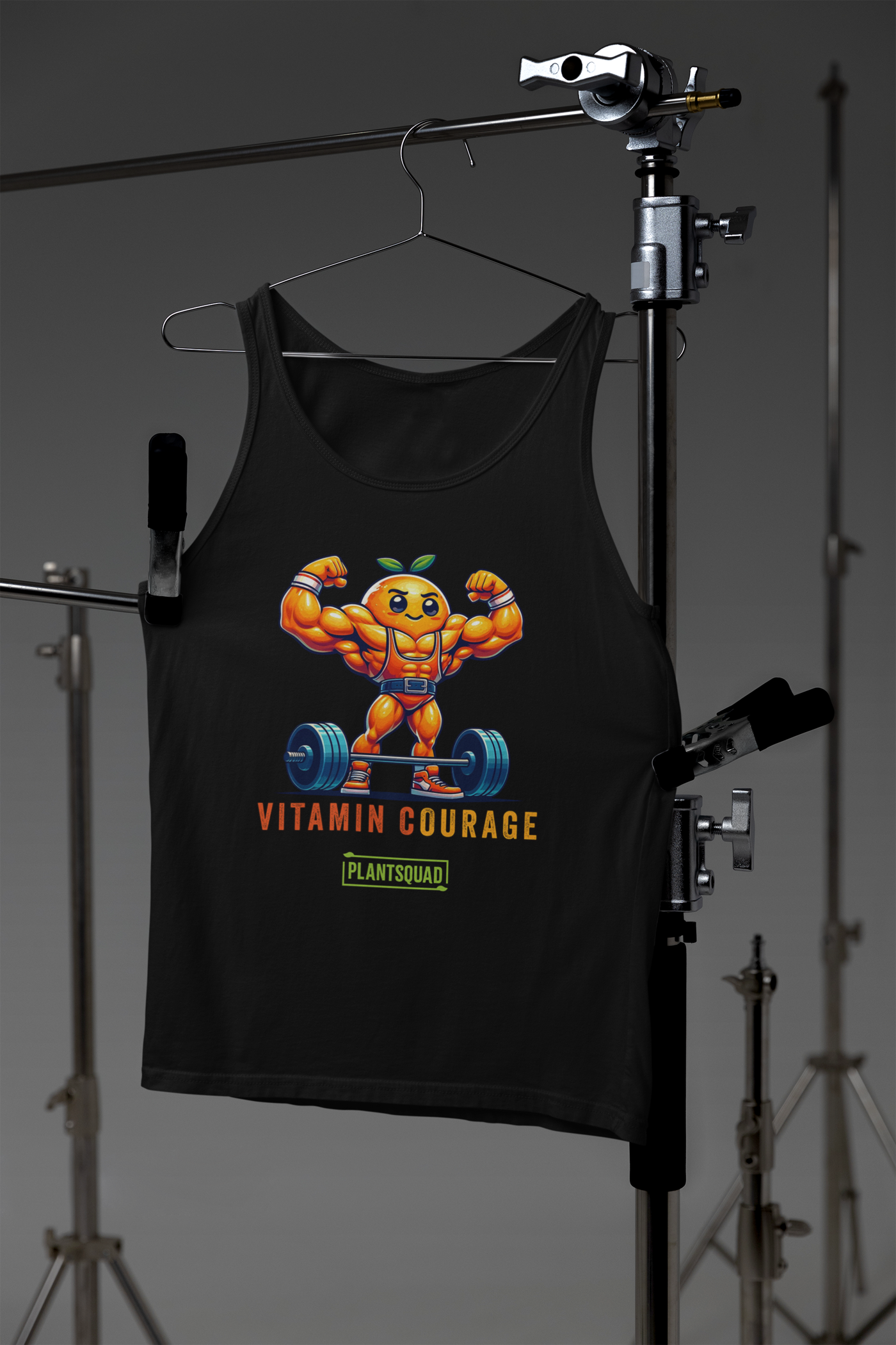 A black gym tank top featuring a muscular orange character lifting a barbell. The character has a determined face, wearing orange shorts and shoes, with a green leaf on its head. The text below reads "VITAMIN COURAGE" and "PLANTSQUAD" with a green rectangular frame around it—perfect for those embracing a vegan workout clothing style. The product is called Plantsquad Orange "Vitamin Courage" - Unisex Tank Top.