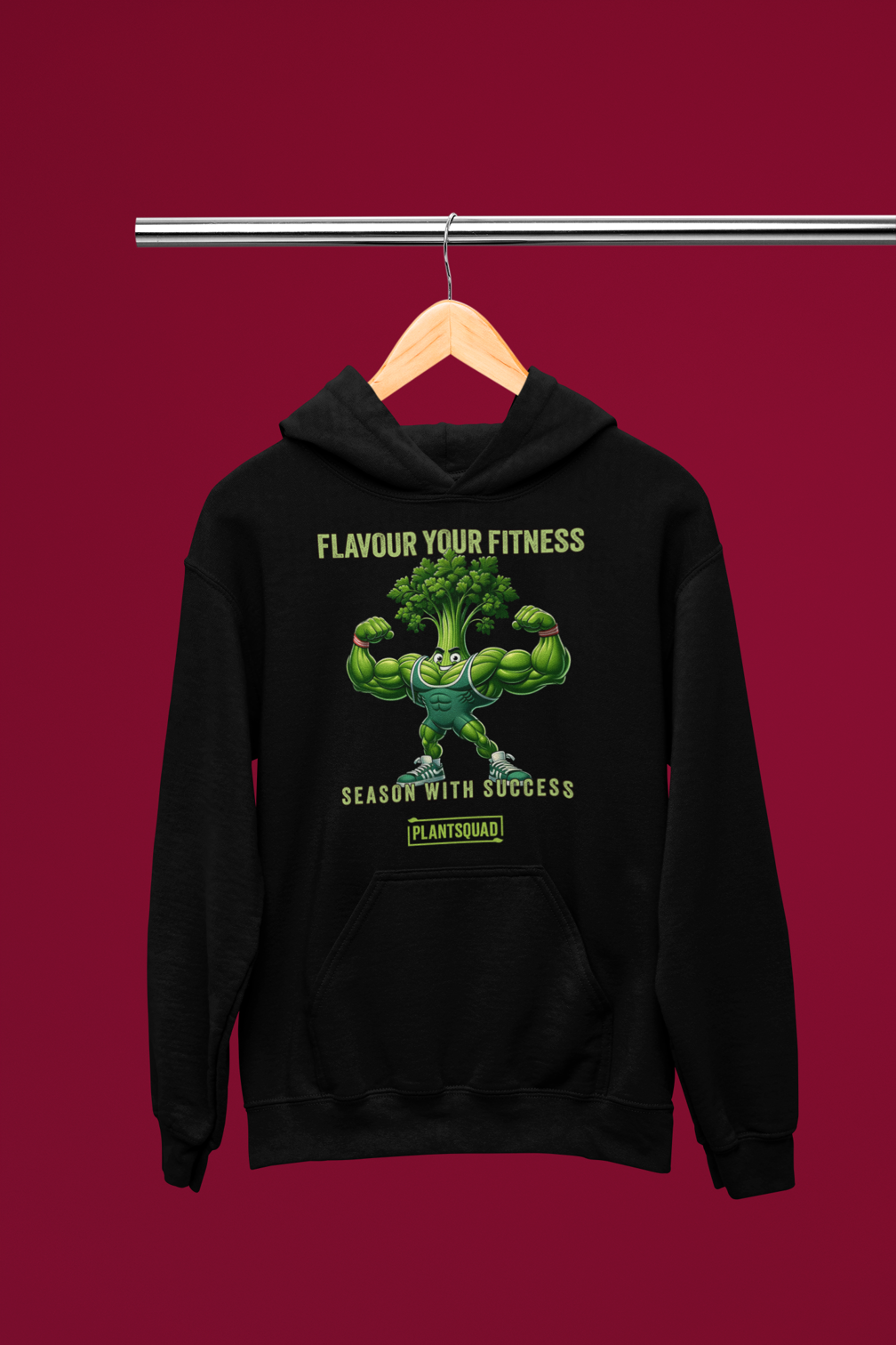 A black vegan hoodie featuring a muscular, anthropomorphic broccoli character flexing its arms. Above the character, the text reads "Flavour Your Fitness," and below it says "Season With Success." The "PLANTSQUAD" logo is displayed at the bottom, perfect for plant-based fitness enthusiasts. This is the Plantsquad Parsley "Flavour Your Fitness Season With Success" - Unisex Hoodie.