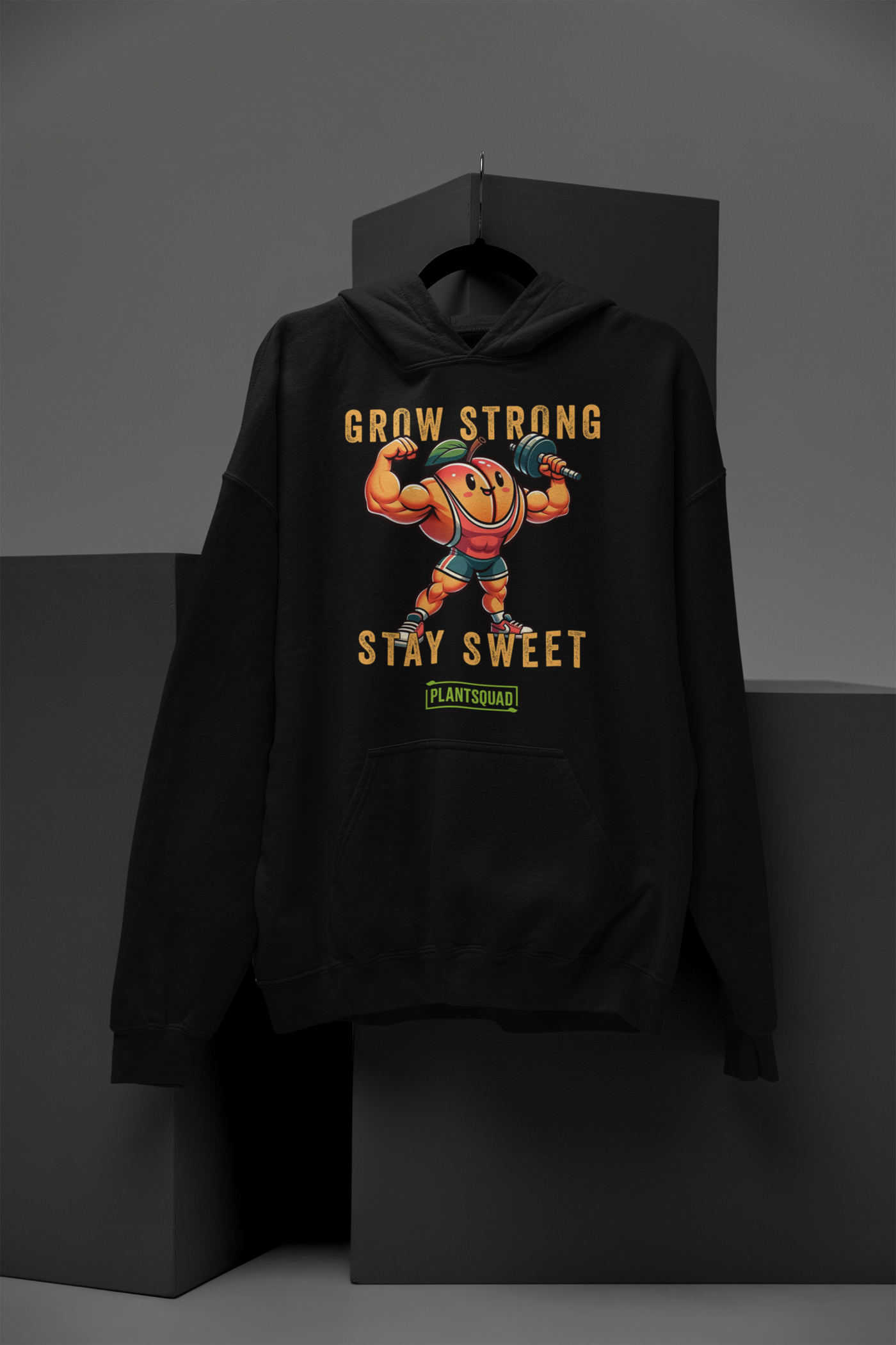 The Plantsquad Peach "Grow Strong Stay Sweet" - Unisex Hoodie features a cheerful, muscular cartoon orange lifting dumbbells. The text above and below the orange reads "Grow Strong Stay Sweet" with a small green label at the bottom that says "PLANTSQUAD." Made from cozy fabric, it's perfect for promoting a vegan lifestyle.