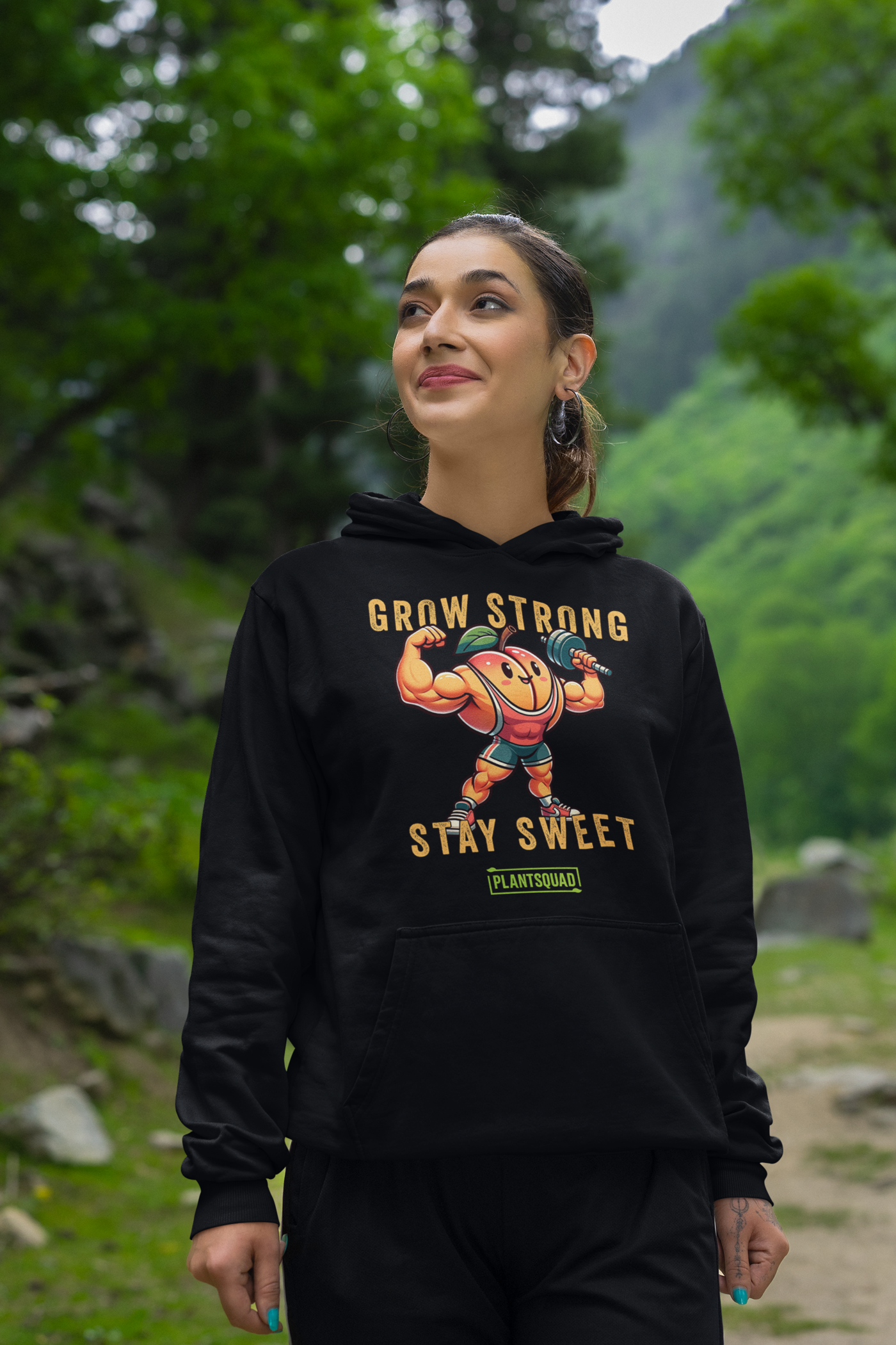 The Plantsquad Peach "Grow Strong Stay Sweet" - Unisex Hoodie features a cheerful, muscular cartoon orange lifting dumbbells. The text above and below the orange reads "Grow Strong Stay Sweet" with a small green label at the bottom that says "PLANTSQUAD." Made from cozy fabric, it's perfect for promoting a vegan lifestyle.