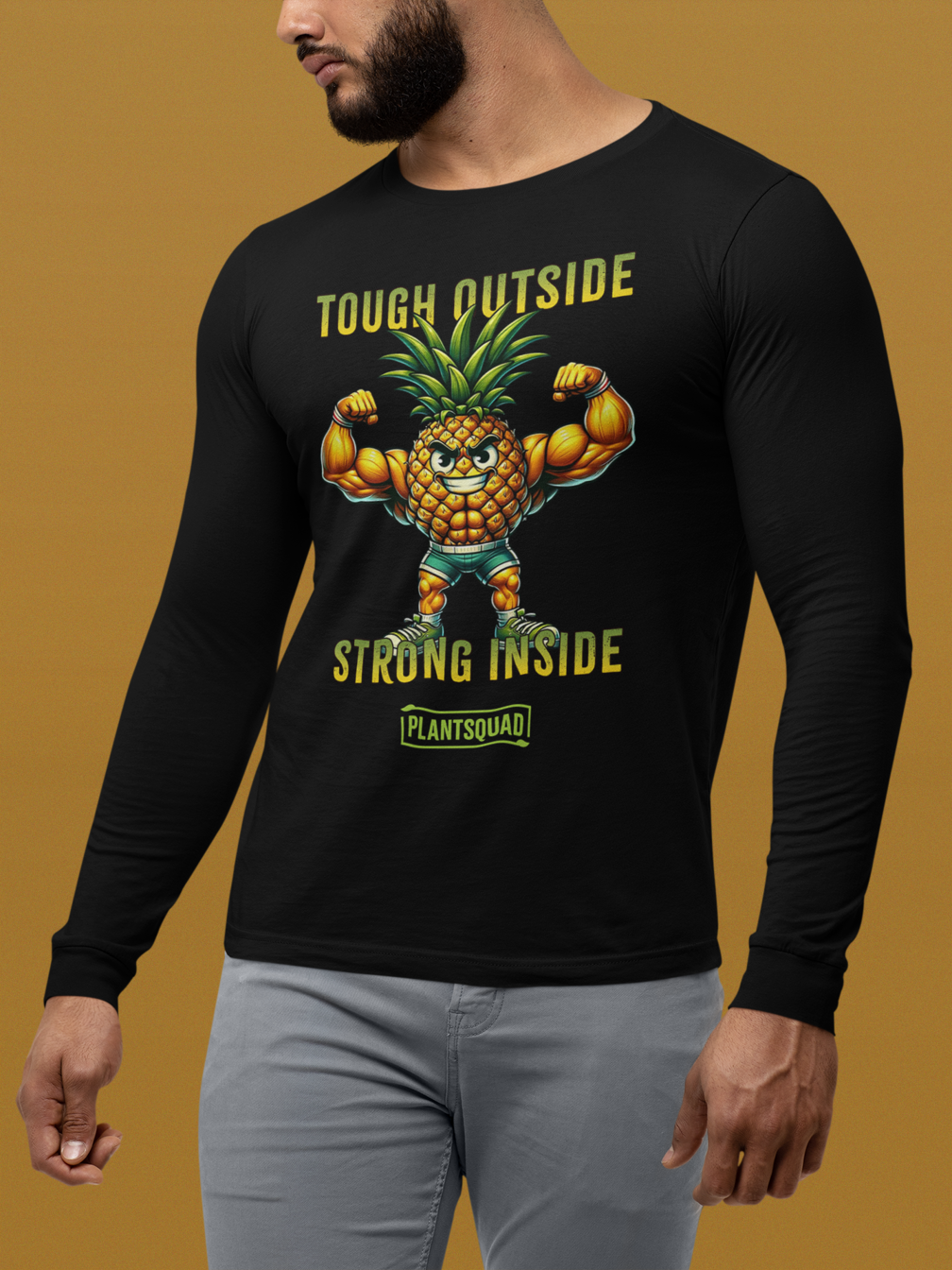 A black Plantsquad Pineapple "Tough Outside Strong Inside" - Unisex Long Sleeve T-Shirt features a muscly pineapple cartoon flexing with a fierce expression. The text "Tough Outside, Strong Inside" is printed above and below it, and "Plantsquad" is written at the bottom, celebrating a plant-based lifestyle and vegan fitness.