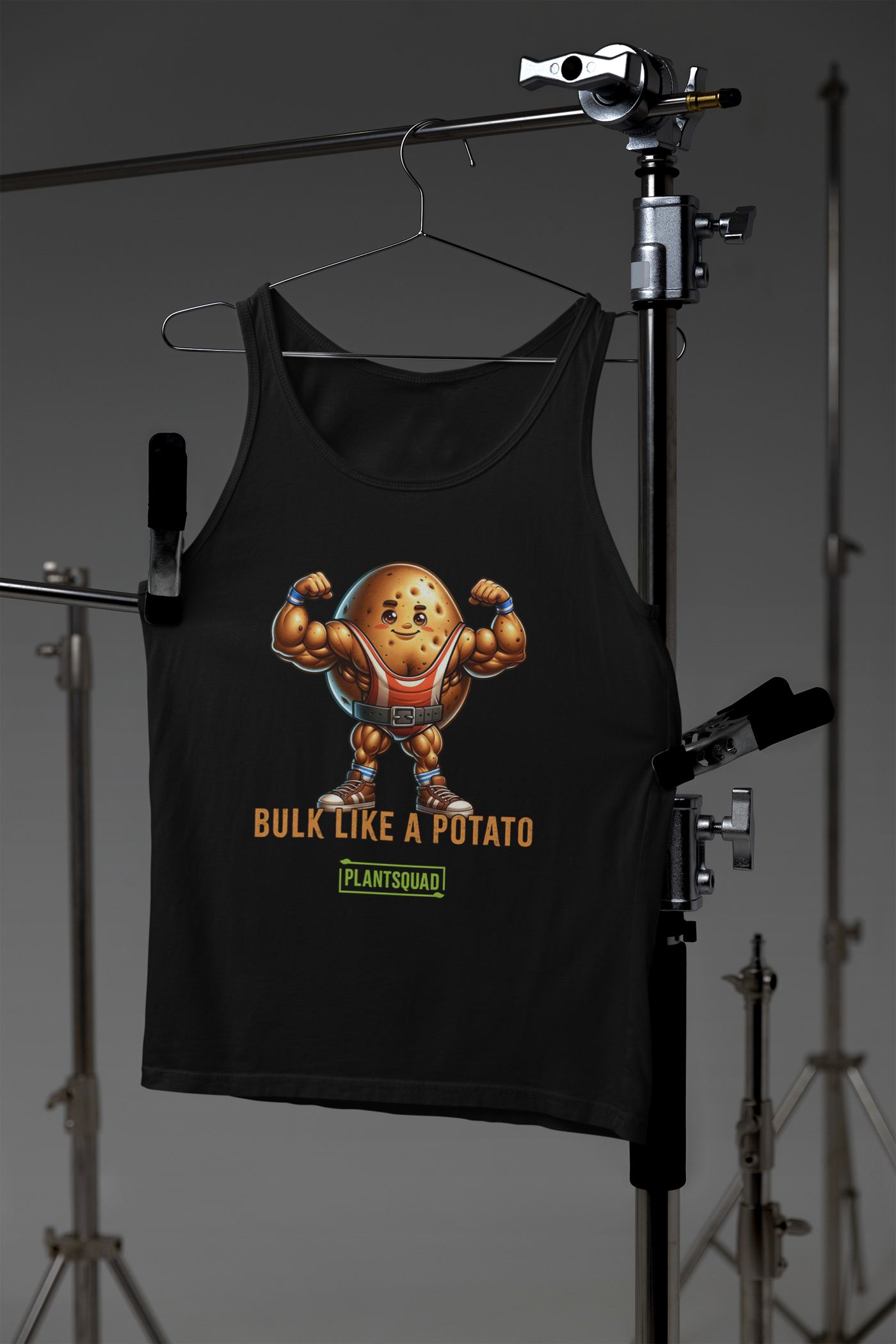 A black gym tank top features a muscular, cartoon potato lifting weights. The text below the potato reads, "BULK LIKE A POTATO," and underneath, "PLANTSQUAD" is written in green. This Plantsquad Potato "Bulk Like A Potato" - Unisex Tank Top is perfect for plant-based fitness enthusiasts.