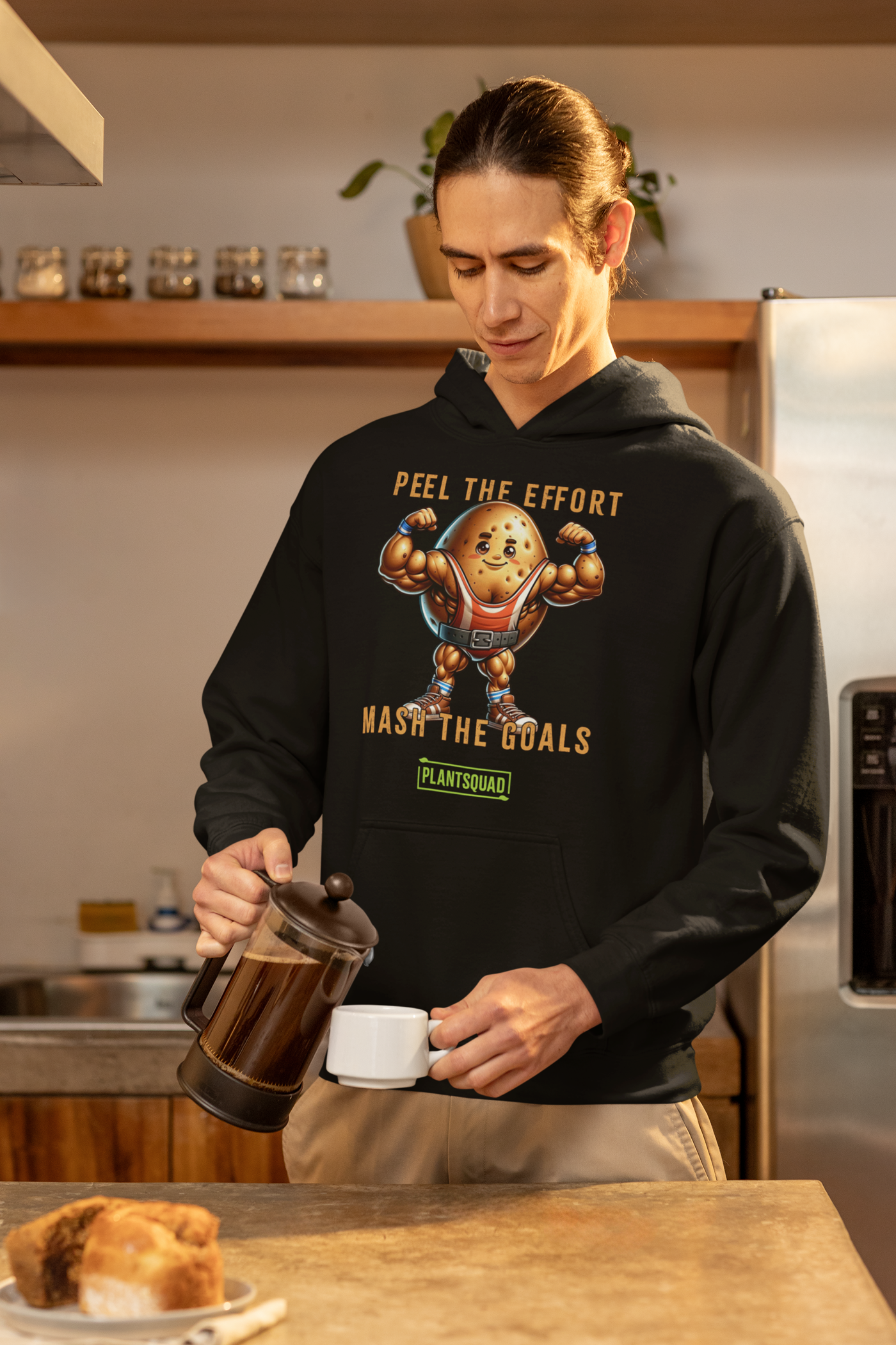 The Plantsquad Potato "Peel The Effort Mash The Goals" - Unisex Hoodie features a muscular potato character lifting weights. Above and below the potato, texts read "Peel The Effort" and "Mash The Goals." Promoting a vegan lifestyle, the word "PlantSquad" is displayed beneath the potato graphic.