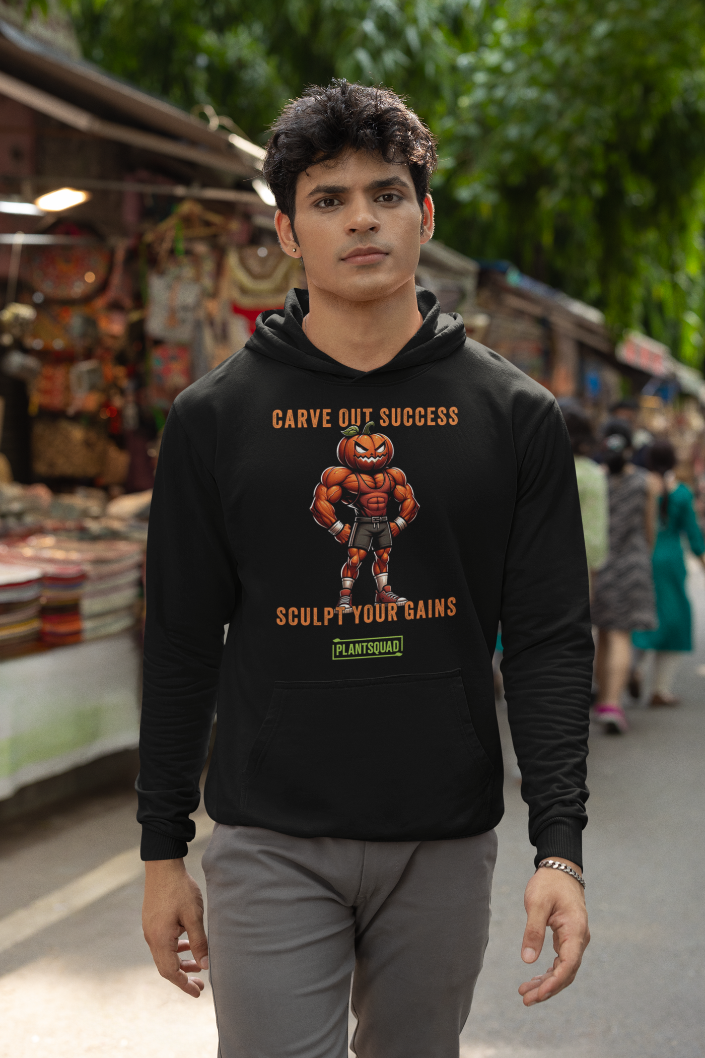 A black weight lifting hoodie features an illustration of a muscular pumpkin-headed figure in workout attire. The text above and below reads "Carve Out Success" and "Sculpt Your Gains," with a small "PlantSquad" logo at the bottom, celebrating the vegan lifestyle. This is the Plantsquad Pumpkin "Carve Out Your Success Sculpt Your Gains" - Unisex Hoodie.