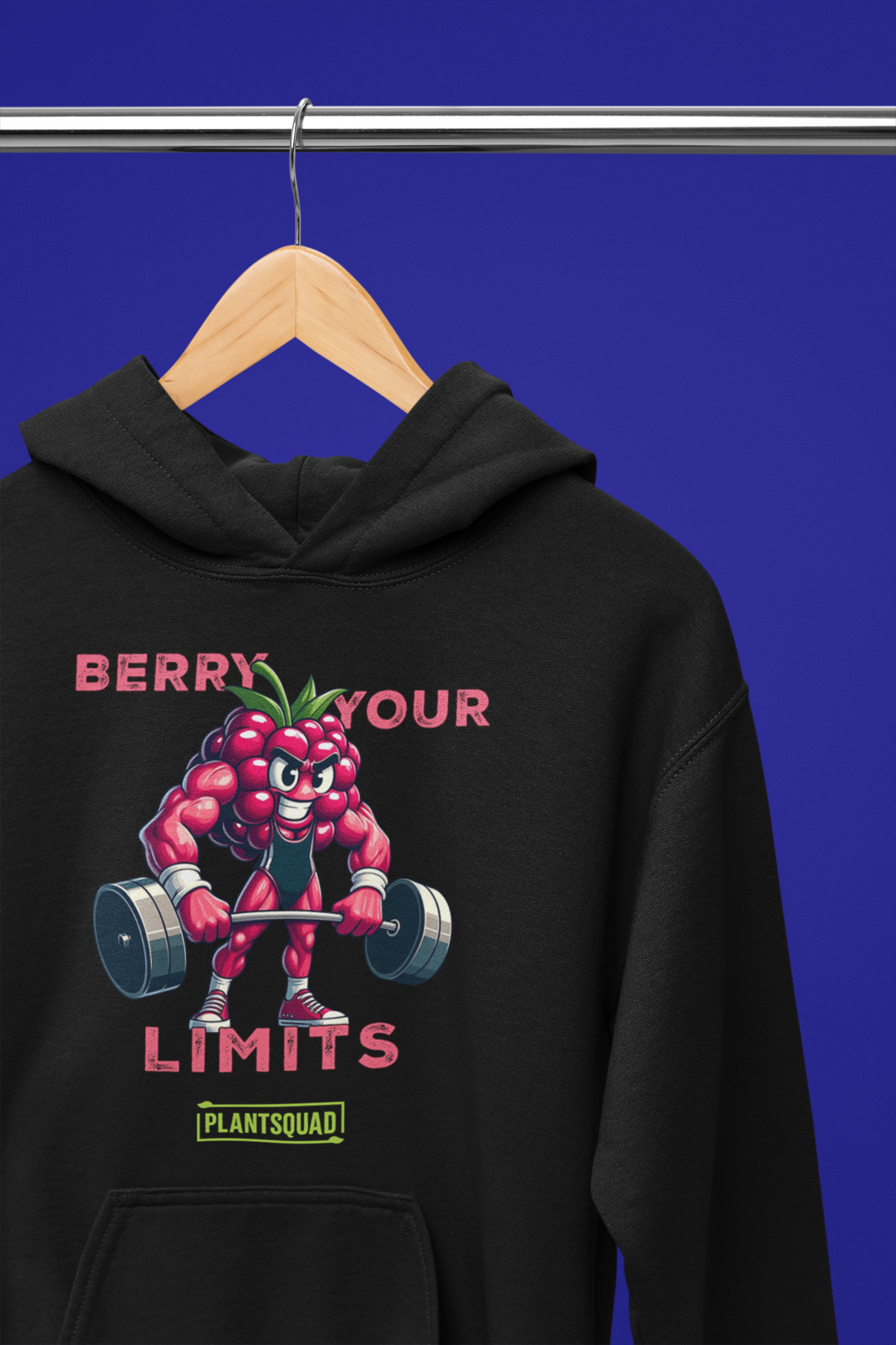 A black hoodie with a printed cartoon image of a muscular strawberry character lifting dumbbells. The text above reads "Berry Your Limits," perfect for those embracing a vegan gym wear style, and "Plantsquad" is written below the character. Introducing the Plantsquad Raspberry "Berry Your Limits" - Unisex Hoodie.