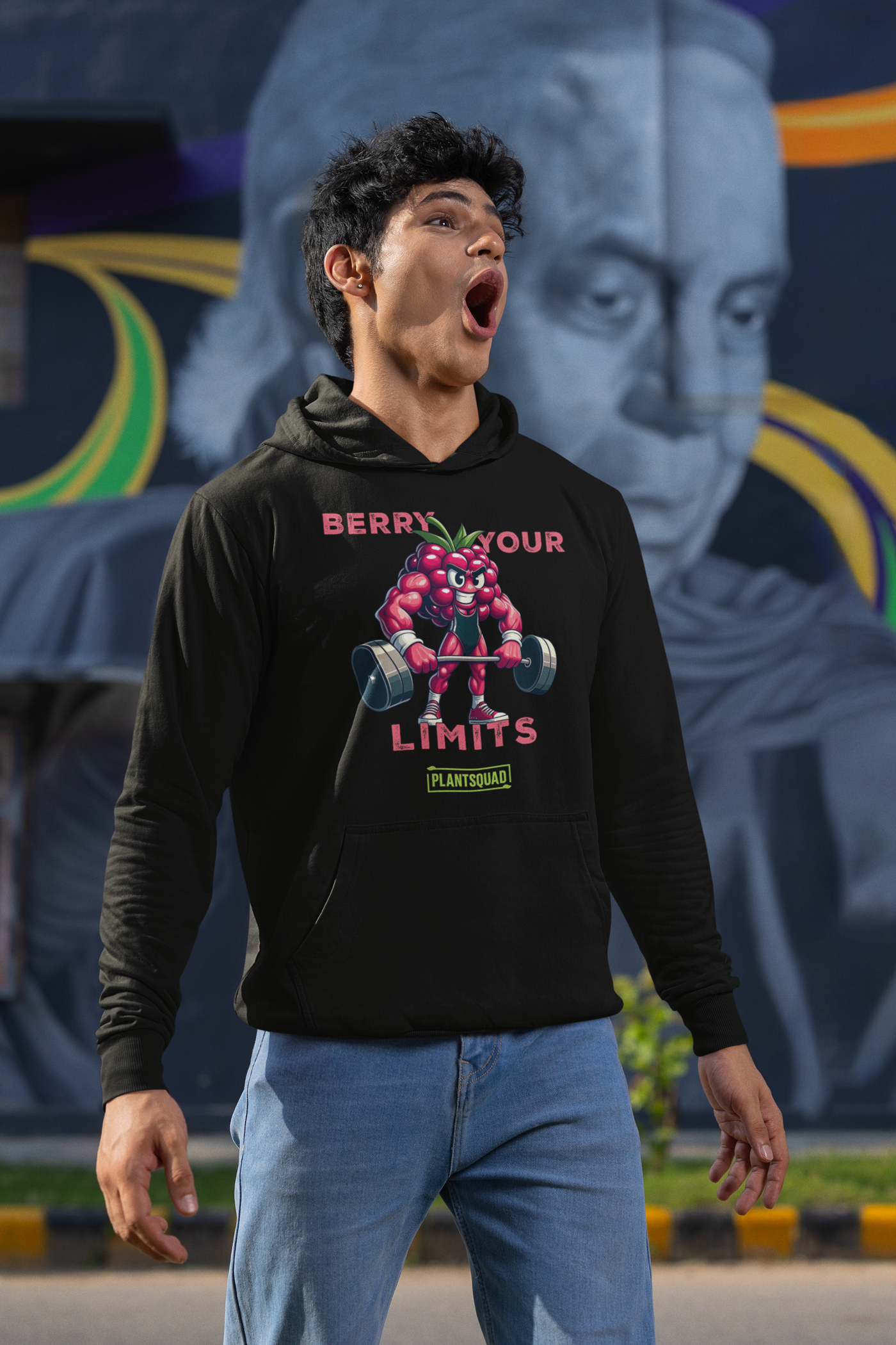 A black hoodie with a printed cartoon image of a muscular strawberry character lifting dumbbells. The text above reads "Berry Your Limits," perfect for those embracing a vegan gym wear style, and "Plantsquad" is written below the character. Introducing the Plantsquad Raspberry "Berry Your Limits" - Unisex Hoodie.