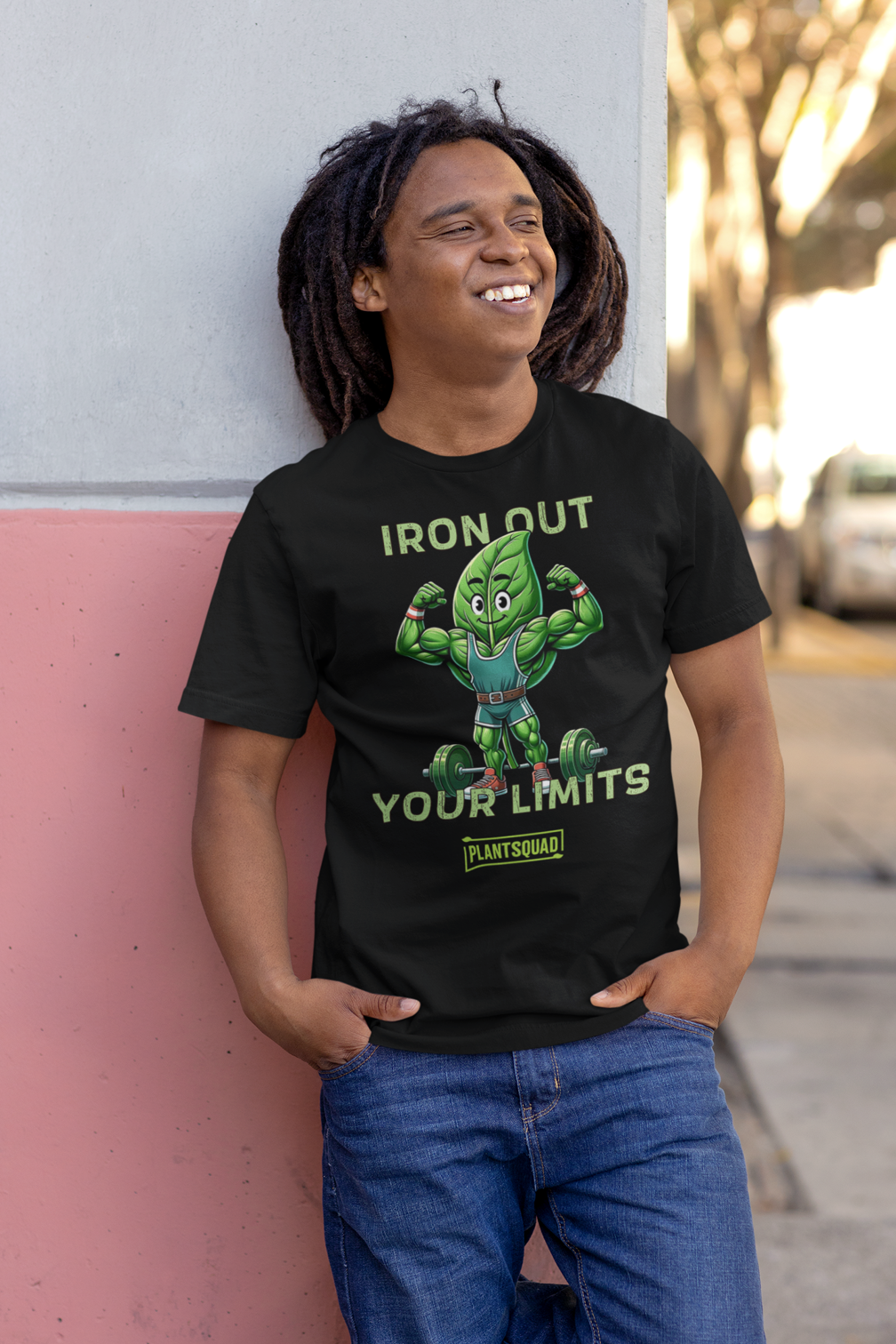 A black Plantsquad Spinach "Iron Out Your Limits" - Unisex T-Shirt featuring a muscular cartoon green leaf character lifting a barbell, with the text "IRON OUT YOUR LIMITS" above and below the character. Embrace your vegan lifestyle with the word "PLANTSQUAD" at the bottom in a small rectangular green box.