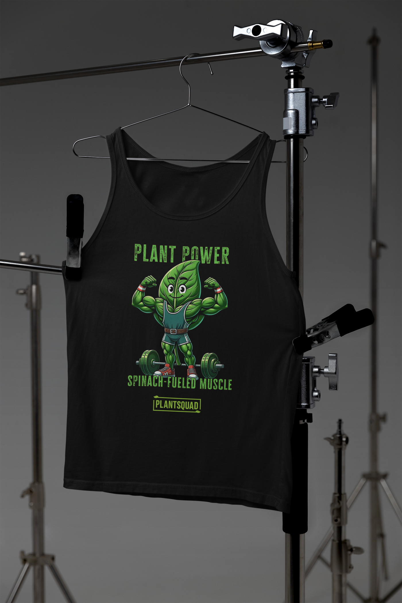 A Plantsquad Spinach "Plant Power Spinach Fueled Muscle" - Unisex Tank Top features a strong cartoon spinach character lifting weights. The text above the character reads "Plant Power," while below it says "Spinach-Fueled Muscle" and "Plantsquad Fitness Apparel." The design promotes a plant-based workout and strength.