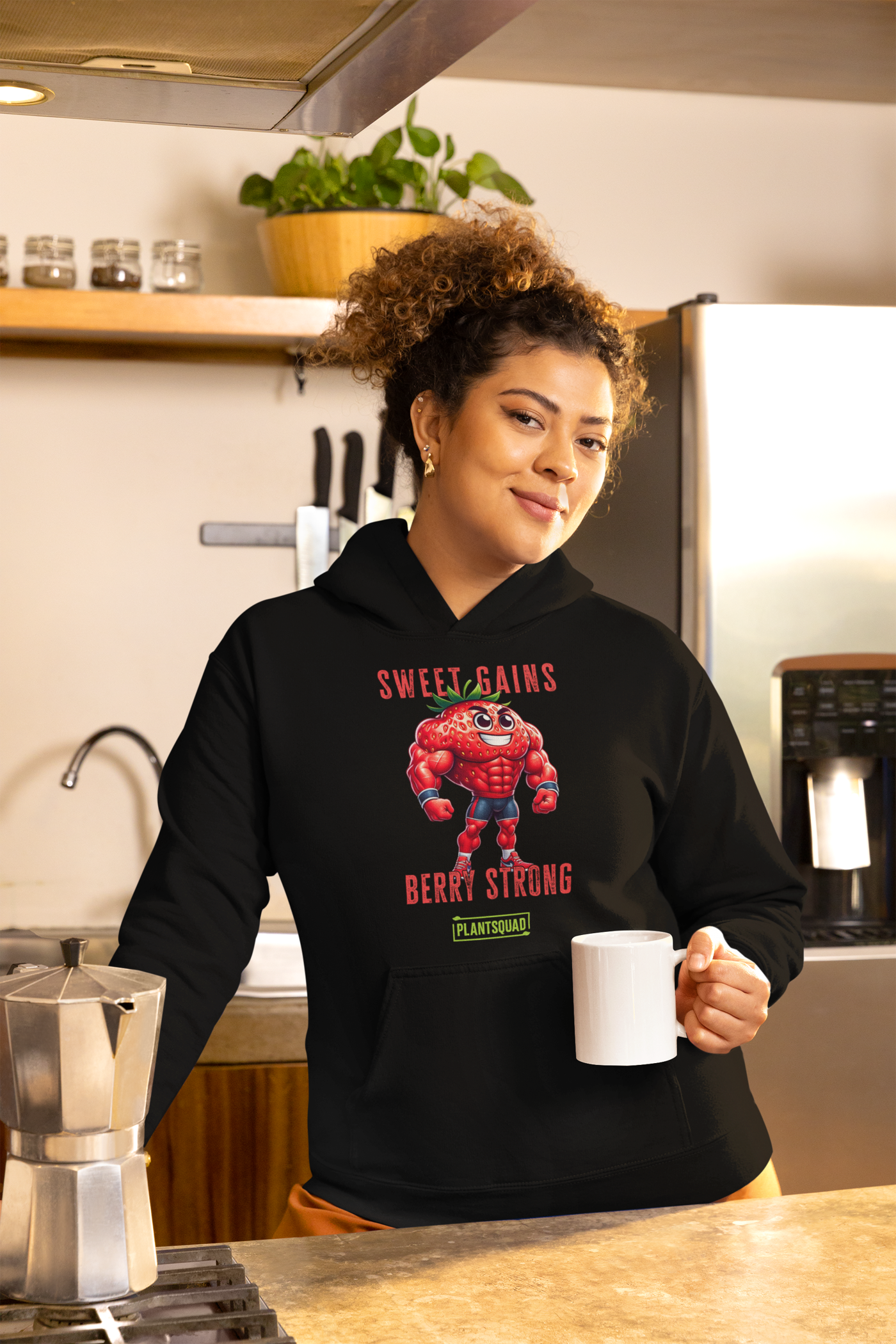 A black Plantsquad Strawberry "Sweet Gains Berry Strong" - Unisex Hoodie featuring a muscular, anthropomorphic strawberry character at the center, perfect for embracing a vegan lifestyle. Text above the strawberry reads "Sweet Gains" and below it reads "Berry Strong" with a small "PlantSquad" logo underneath. Made from cozy fabric, ideal for post-weight lifting comfort.