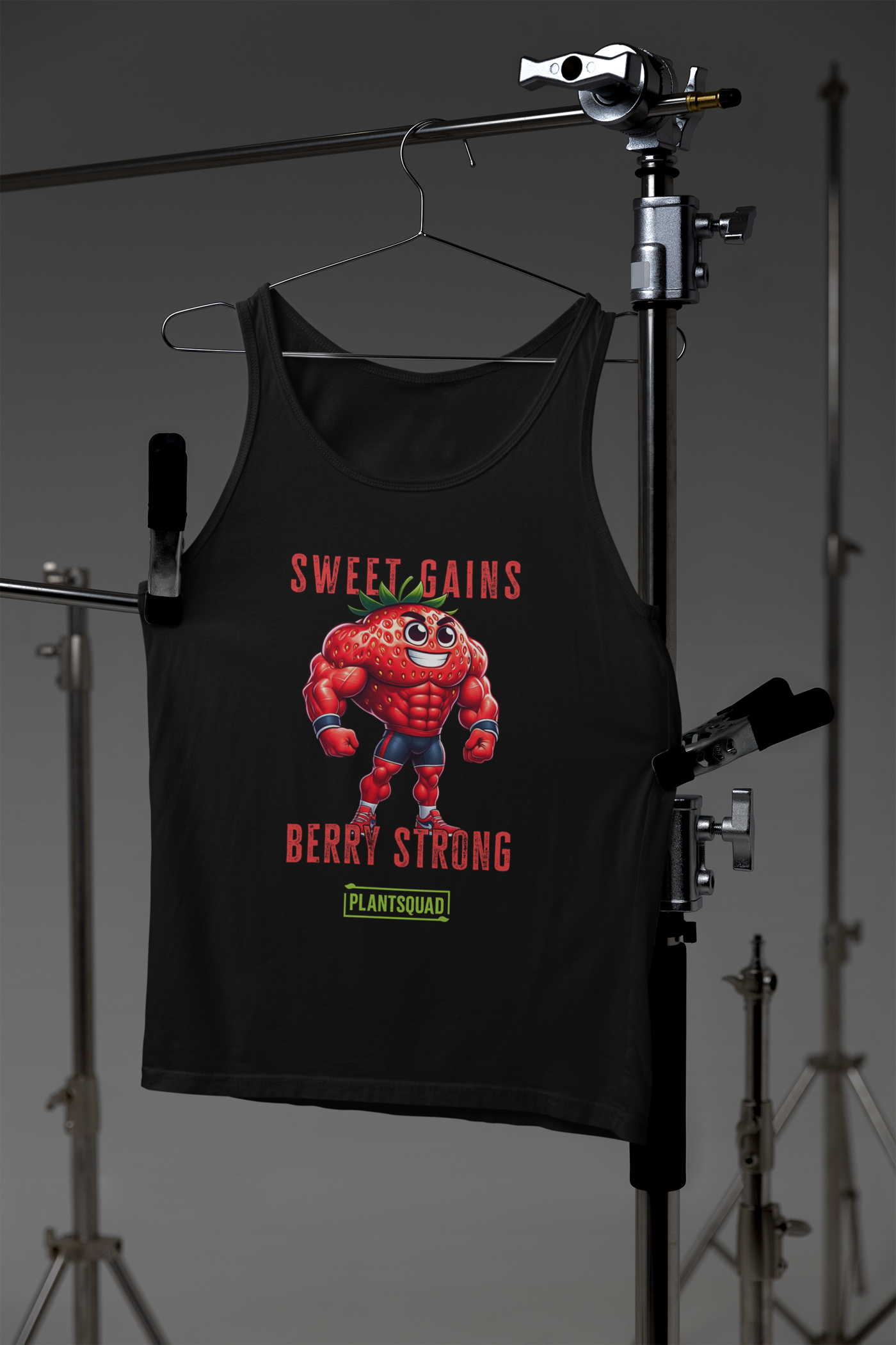 A black Plantsquad Strawberry "Sweet Gains Berry Strong" - Unisex Tank Top featuring a muscular, anthropomorphic strawberry character flexing. Above the strawberry, text reads "Sweet Gains," and below it, "Berry Strong." At the bottom, a green logo with the text "Plantsquad." Perfect for showcasing your plant-based lifestyle in the gym.