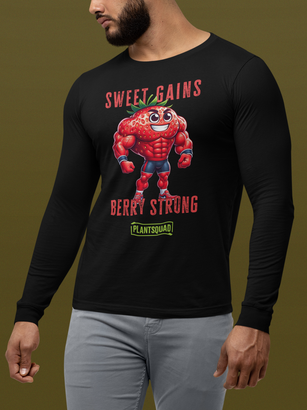 A Plantsquad Strawberry "Sweet Gains Berry Strong" - Unisex Long Sleeve T-Shirt features a muscular, anthropomorphic strawberry flexing its arms. Above and below the strawberry, the text reads "Sweet Gains Berry Strong." Perfect for fitness enthusiasts embracing a vegan lifestyle, the word "PLANTSQUAD" appears in a green box at the bottom of the design.