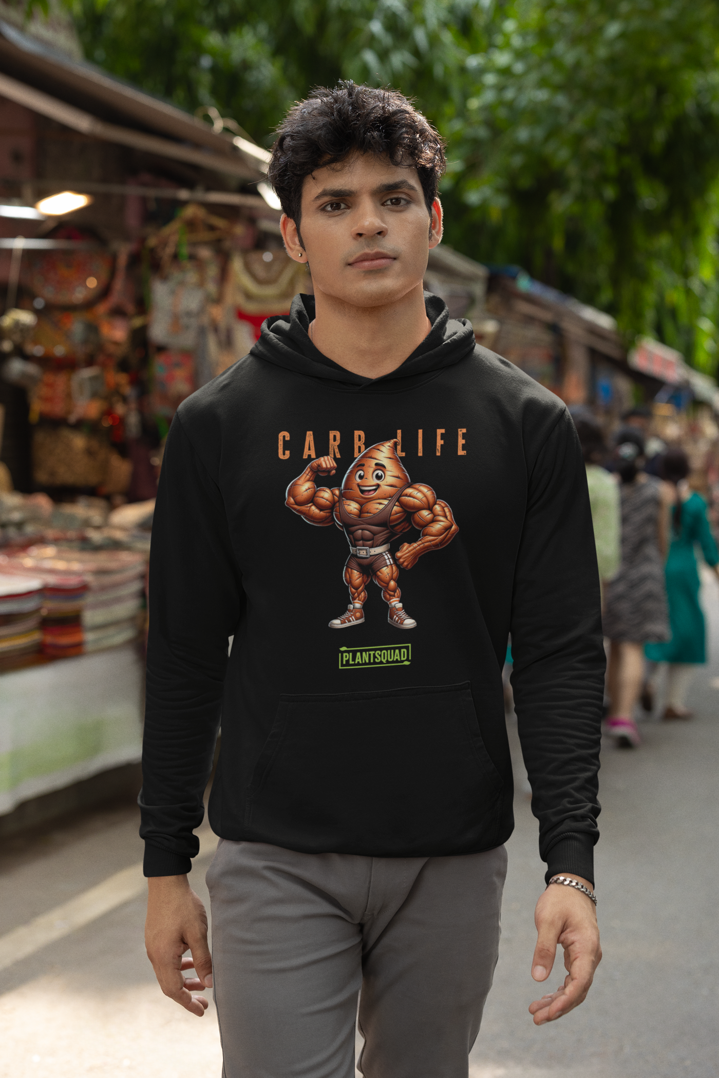 A Plantsquad Sweet Potato "Carb Life" - Unisex Hoodie featuring a cartoon image of a muscular vegetable with a smiling face. Above the image is the text "CARB LIFE" in orange letters, and below it is a green and white logo that reads "PLANTSQUAD." Made from cozy fabric, it's perfect for those embracing a vegan lifestyle.