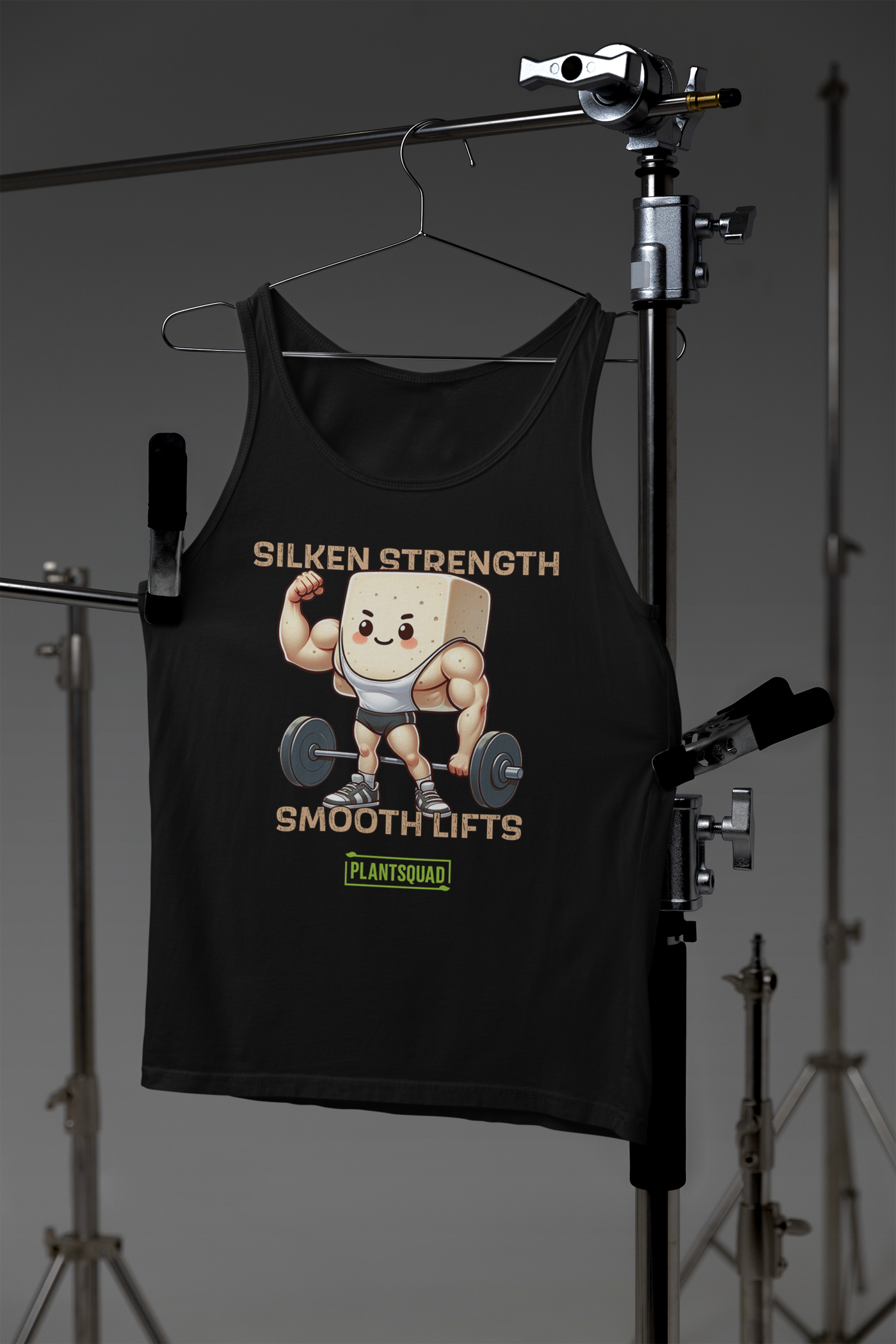 A black Plantsquad Tofu "Silken Strength Smooth Lifts" - Unisex Tank Top featuring a cartoon illustration of a muscular tofu block lifting a barbell. The text above reads "SILKEN STRENGTH," and below it says "SMOOTH LIFTS." Crafted from premium breathable fabric, this tank also has a small green logo with the text "PLANTSQUAD" for your vegan lifestyle.