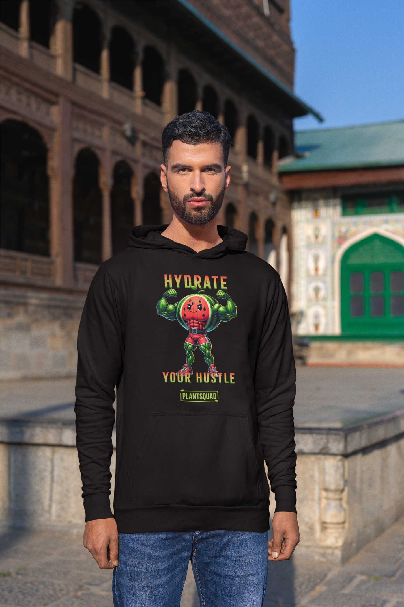 A black workout hoodie features an illustration of a muscular, anthropomorphic watermelon holding two water bottles. The text above and below the illustration reads, "Hydrate Your Hustle." Embrace your plant-based lifestyle with this stylish piece from Plantsquad Watermelon "Hydrate Your Hustle" - Unisex Hoodie.