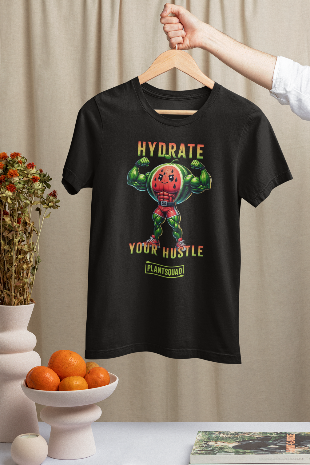 A Plantsquad Watermelon "Hydrate Your Hustle" - Unisex T-Shirt features an illustration of an anthropomorphic watermelon with muscular arms flexing. Above it, the text reads "Hydrate Your Hustle," and below, there's a logo for "Plantsquad." Embrace your vegan fitness in style as the watermelon character rocks a red singlet and green boots.